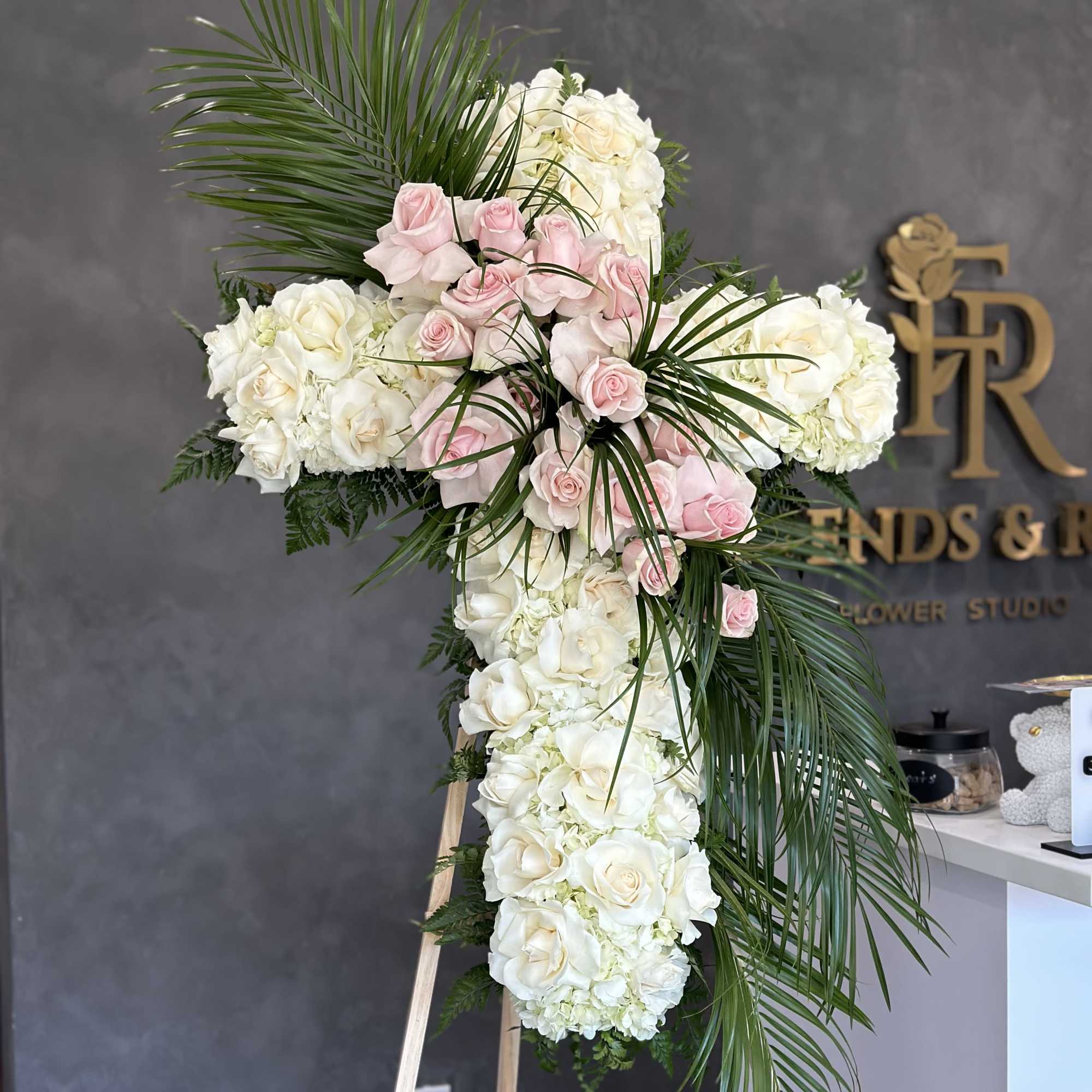 Cross-shaped floral tribute with white and pink roses on an easel