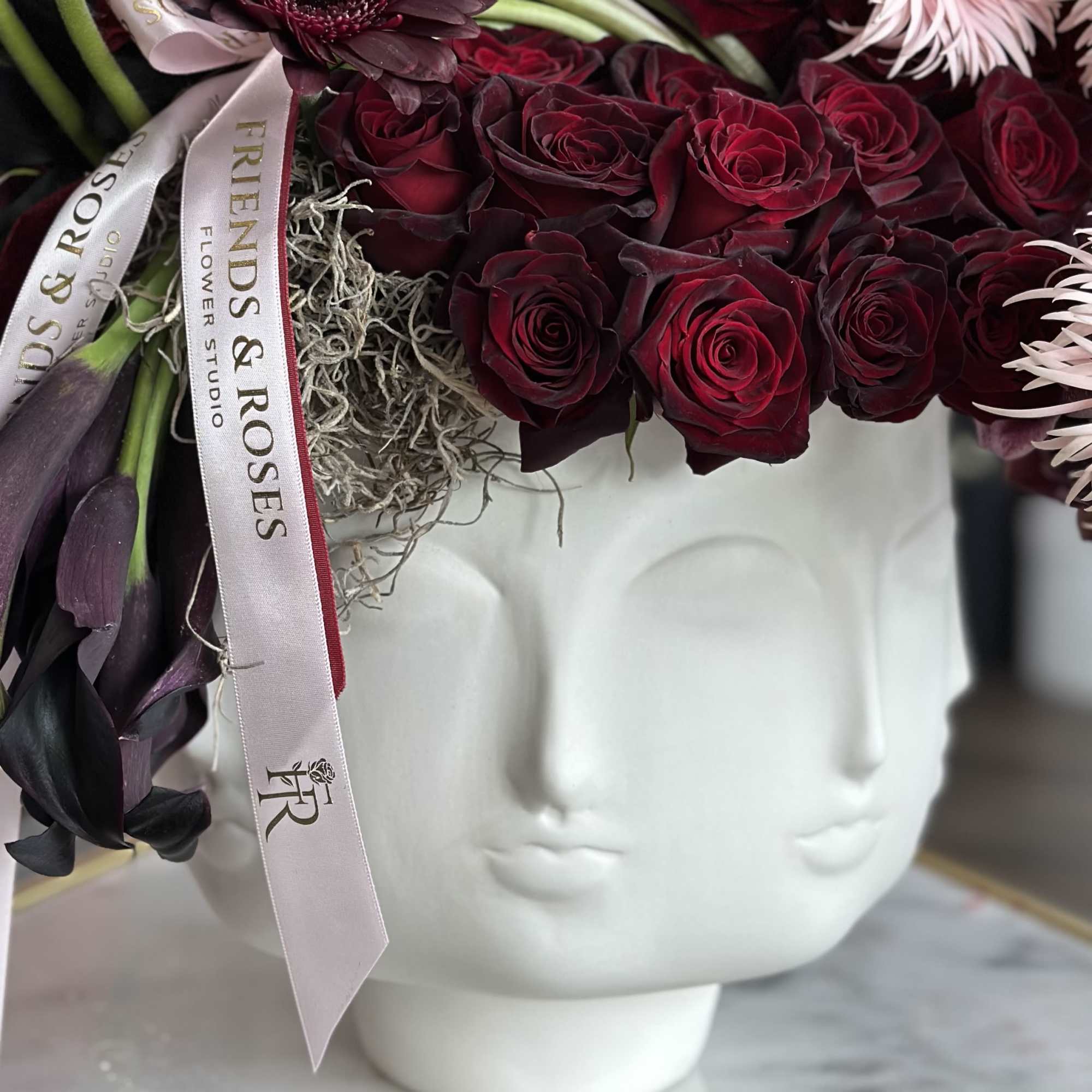 Deep red roses arranged in a white face-shaped vase with a ribbon.
