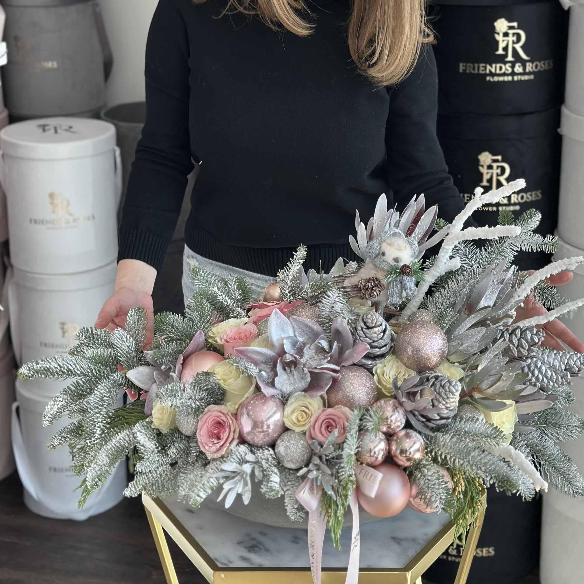 Winter floral arrangement with pink roses, frosted greenery, and ornaments in a low container