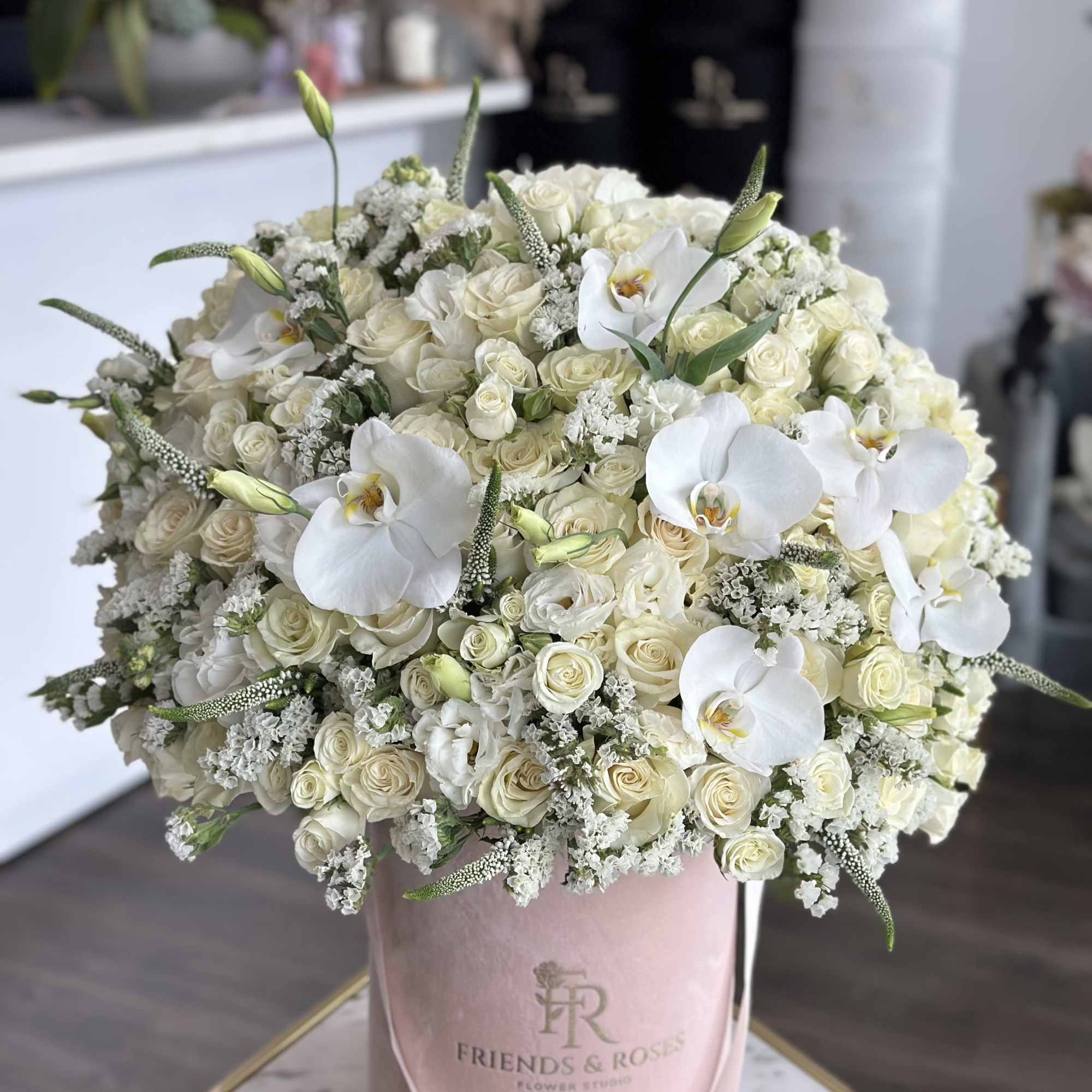 Large white rose and orchid arrangement in a pink hatbox