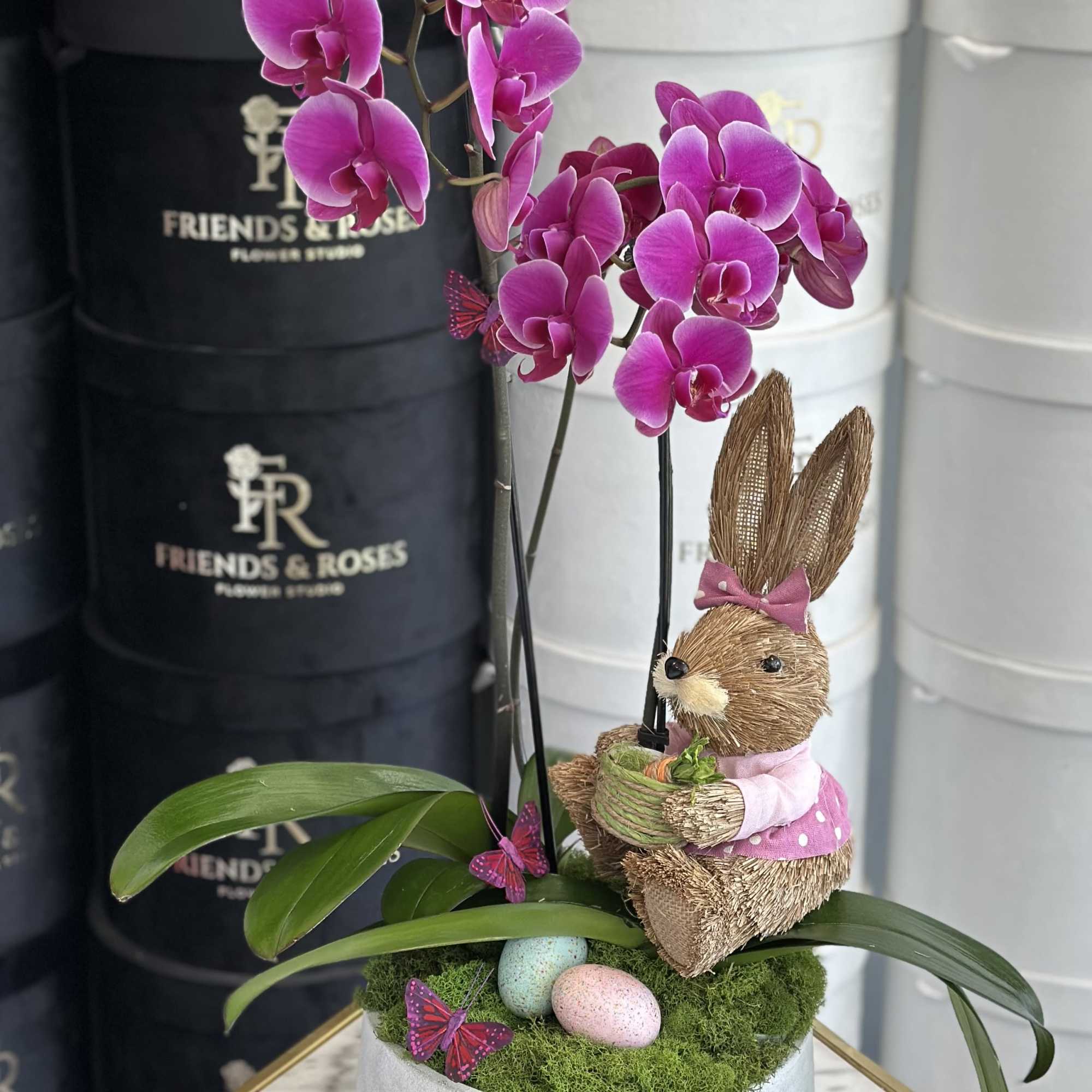 Pink orchid arrangement with a straw bunny and pastel eggs in a round box