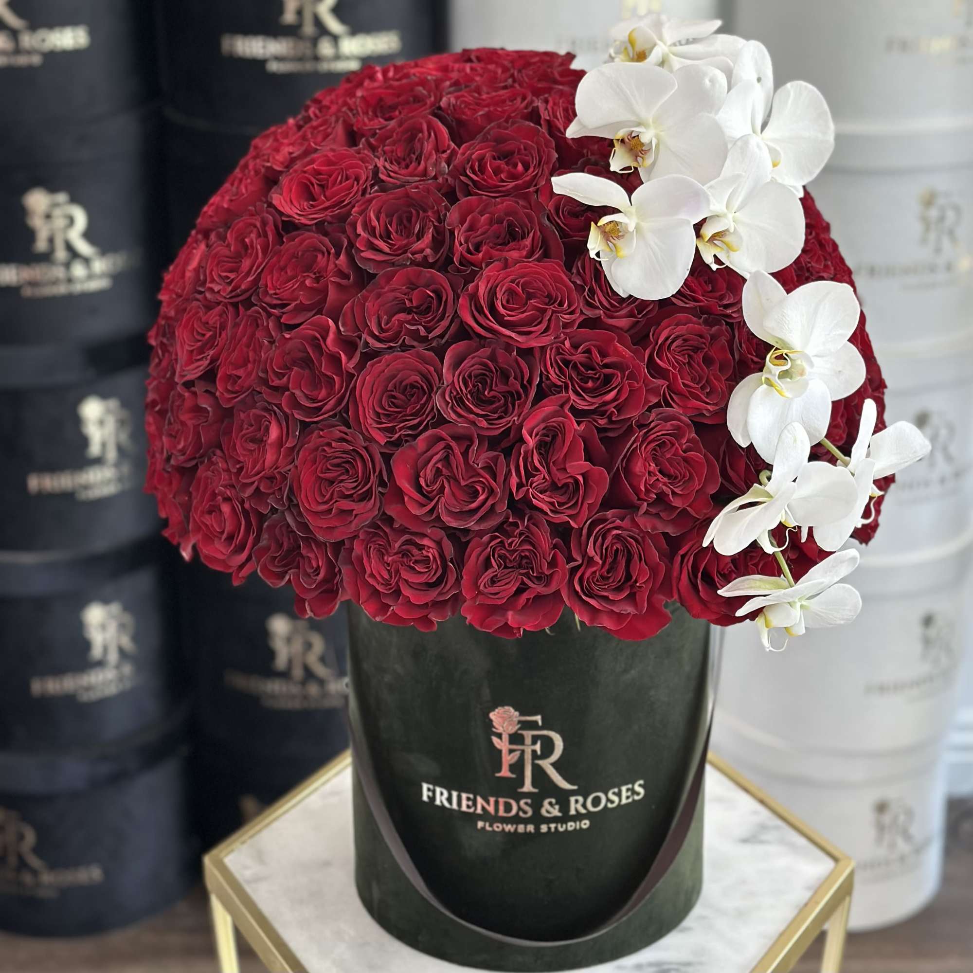 Round bouquet of red roses with white orchids in a dark hat box