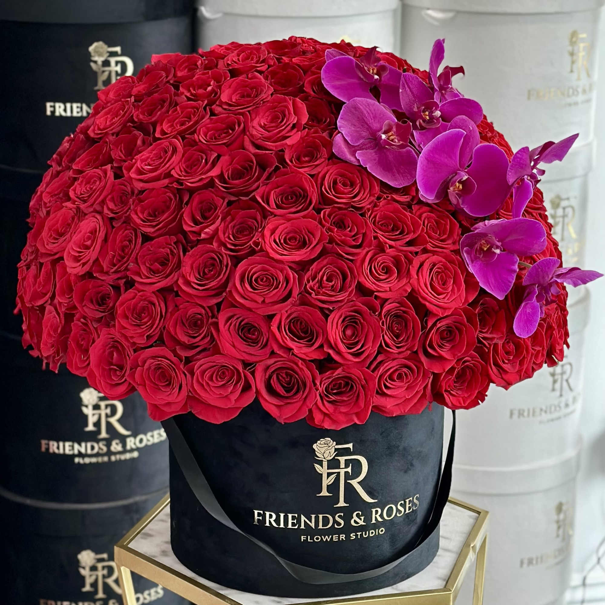 Large red rose arrangement with purple orchids in a black hat box