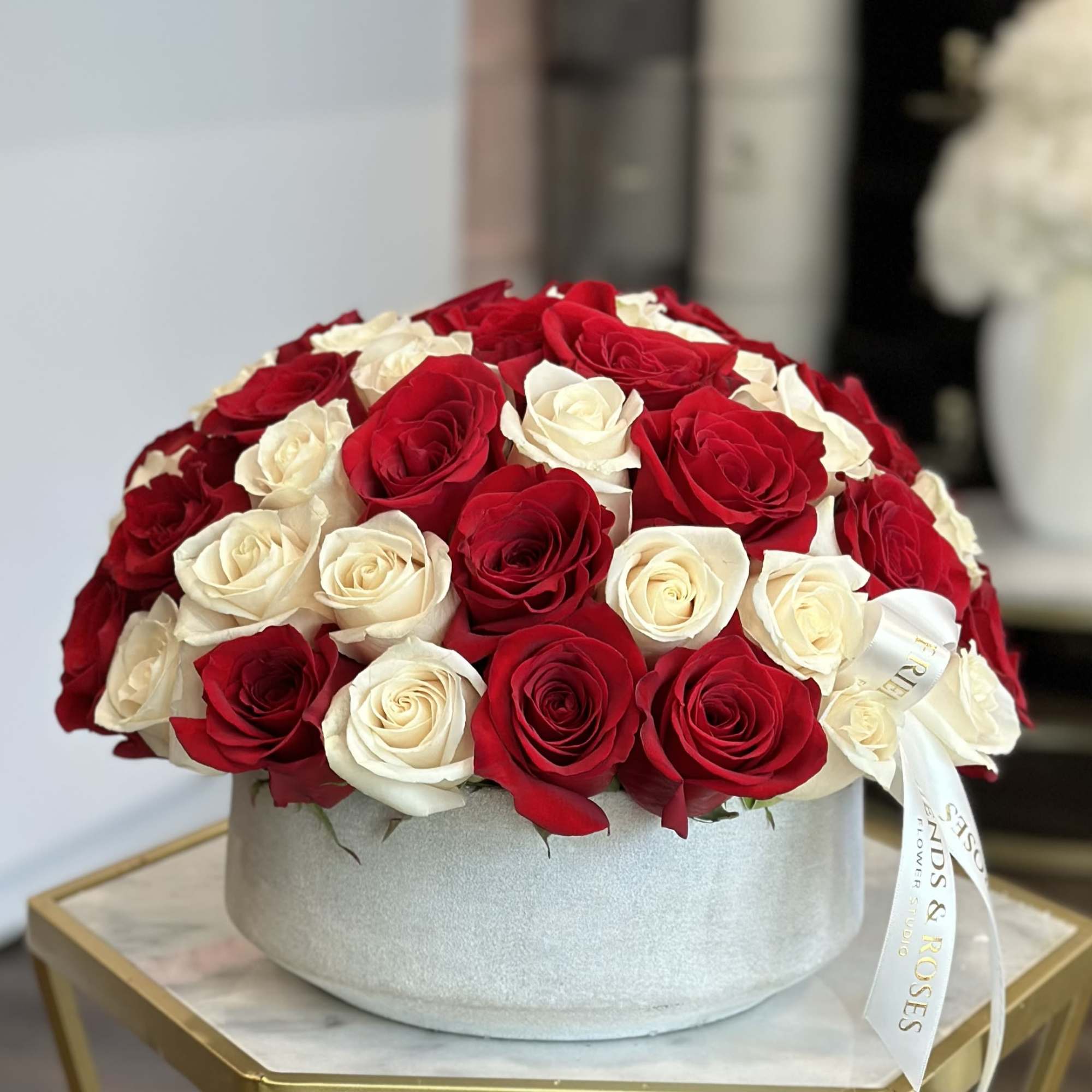 Red and white roses arranged in a round hatbox with a ribbon
