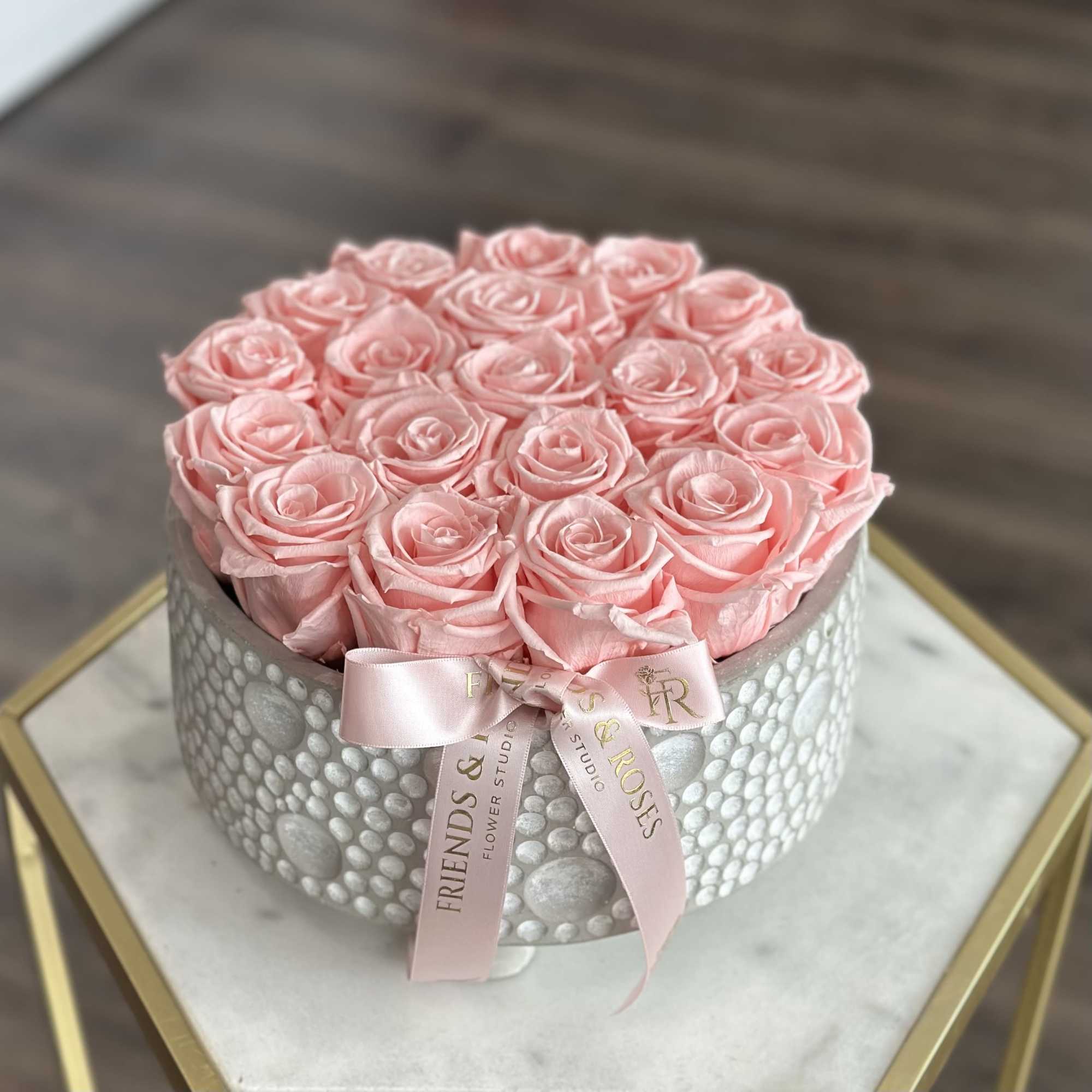 Pink roses arranged in a round hatbox with a pink ribbon.