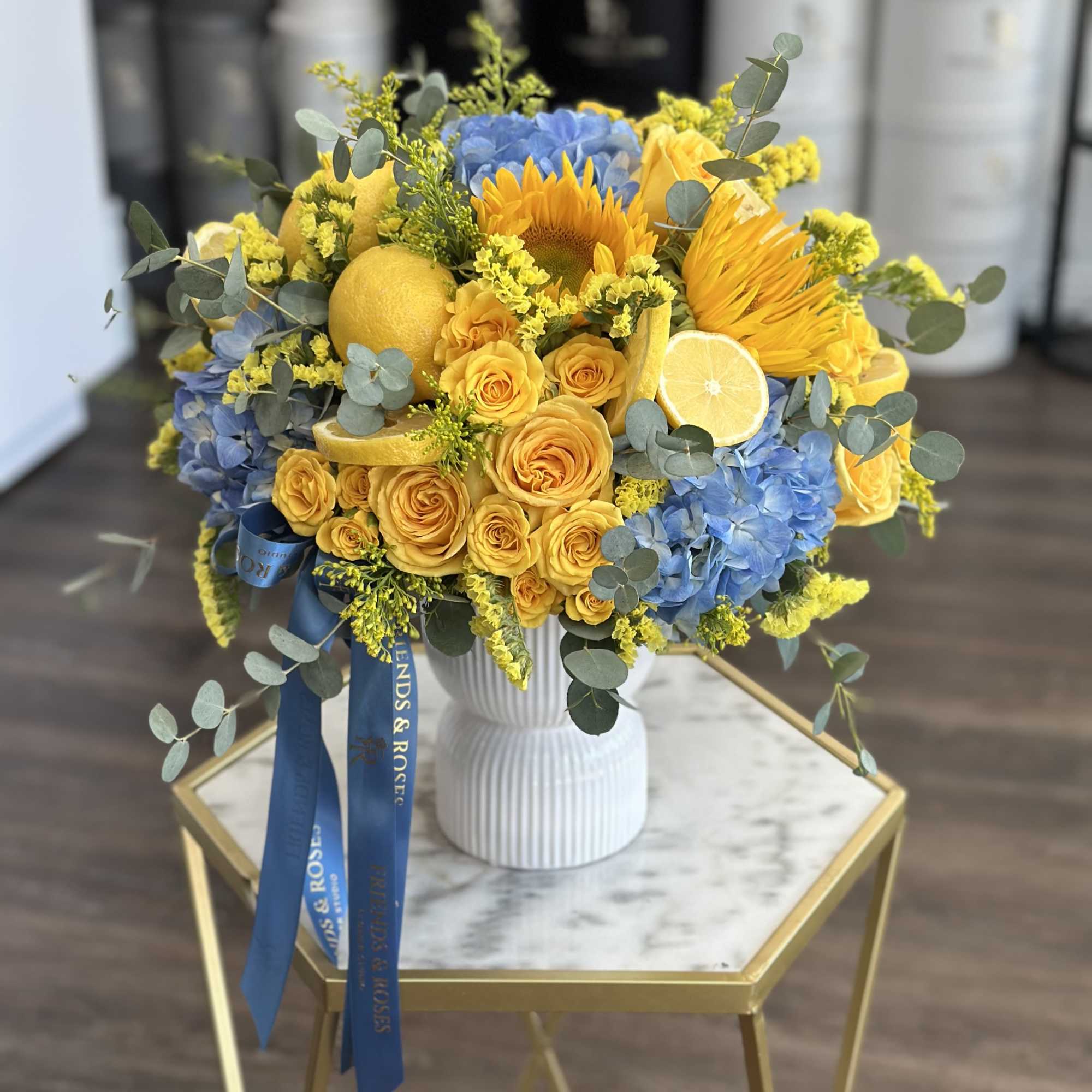 Bouquet of yellow roses, blue hydrangeas, and sunflowers in a white vase