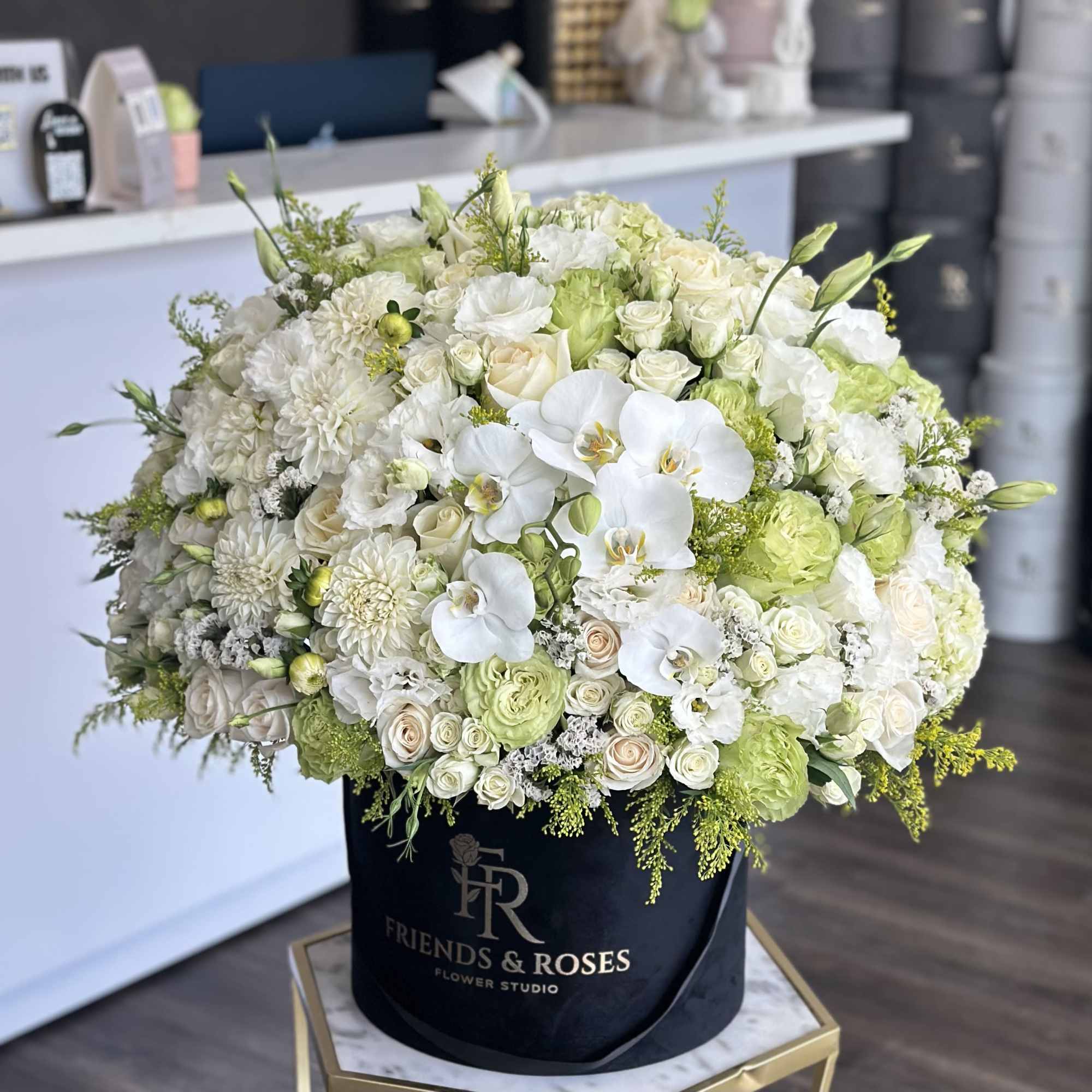 Large white and pale green floral arrangement in a black hatbox