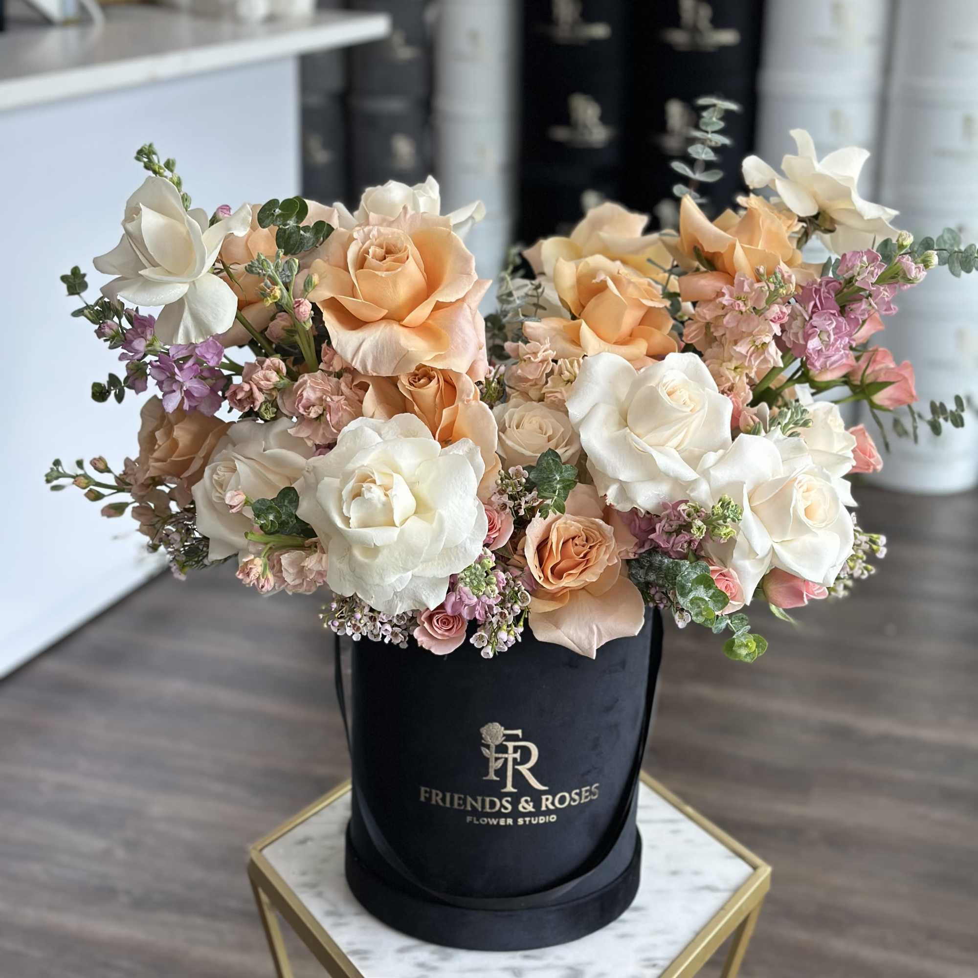 Peach and white roses arranged in a black hat box