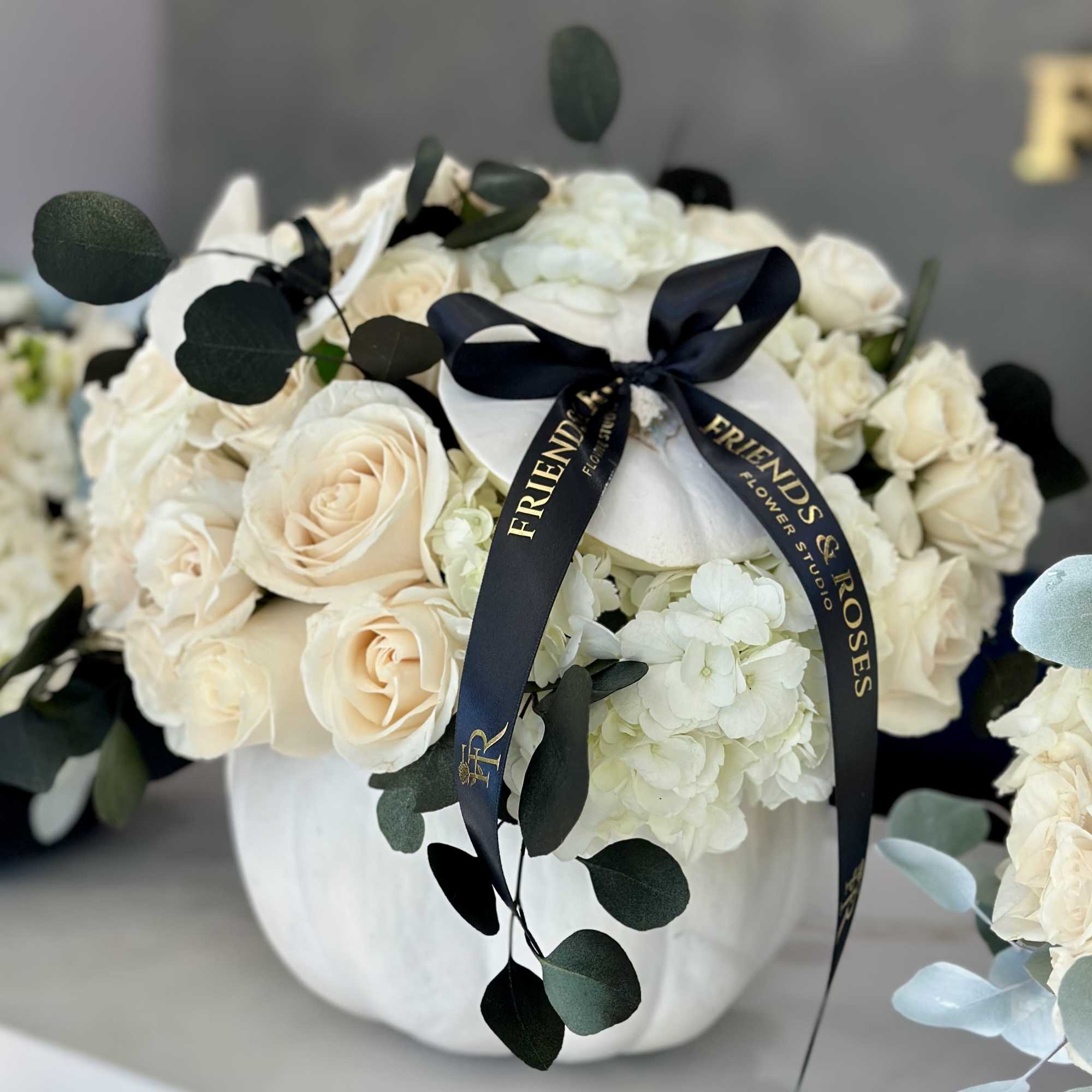 Cream roses and white hydrangeas in a white vase with a dark ribbon