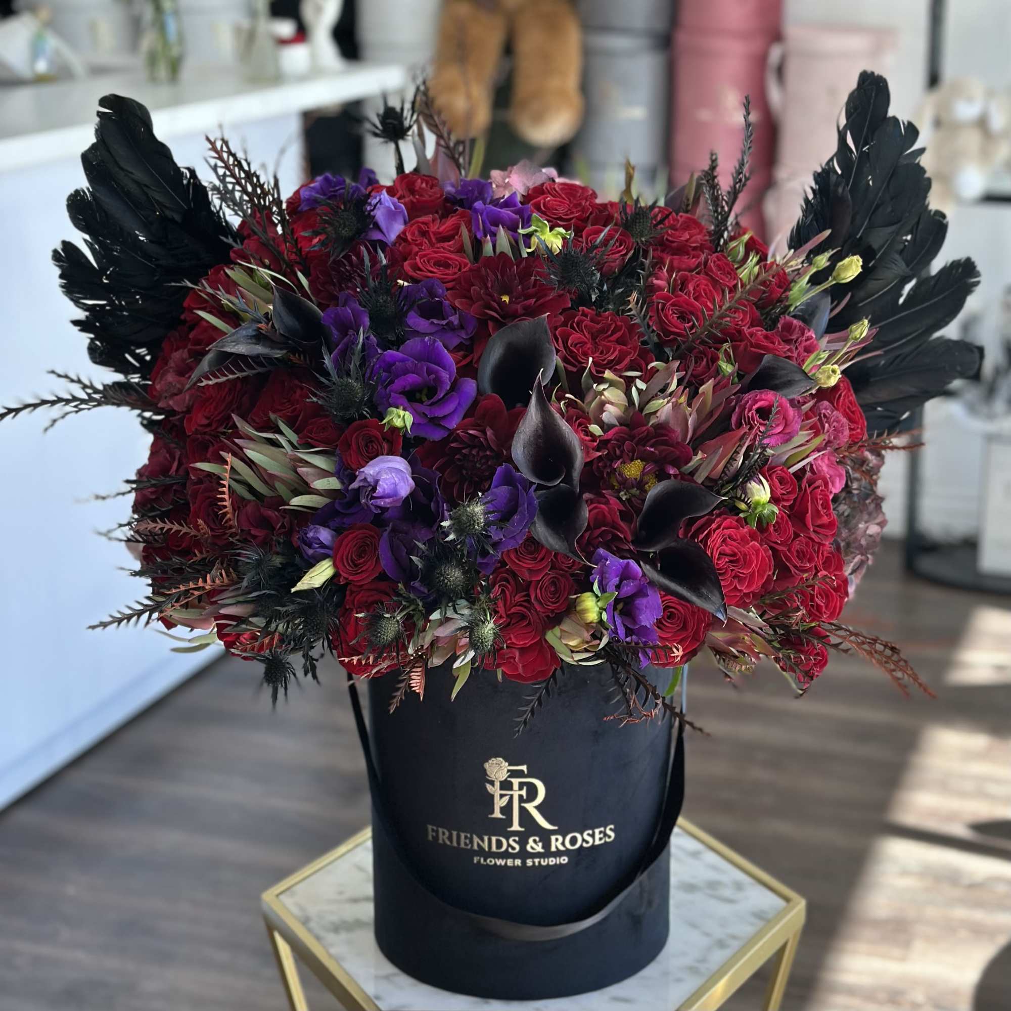 Red and purple floral arrangement in a black hatbox with black feathers