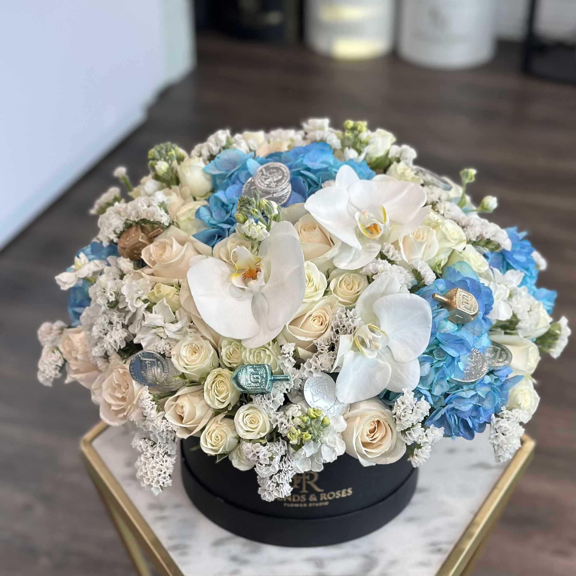 Round bouquet of white orchids, cream roses, and blue hydrangeas in a black box