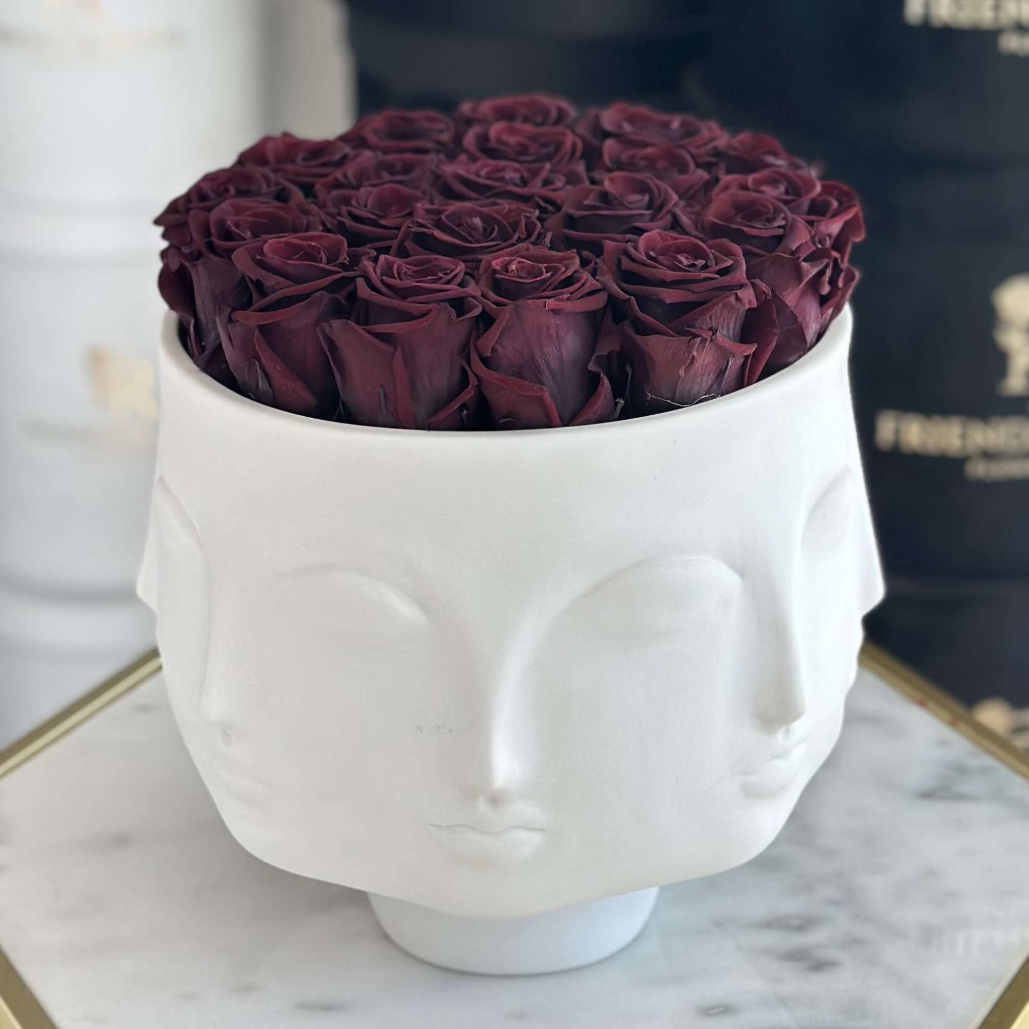 Deep burgundy roses arranged in a white sculptural face vase