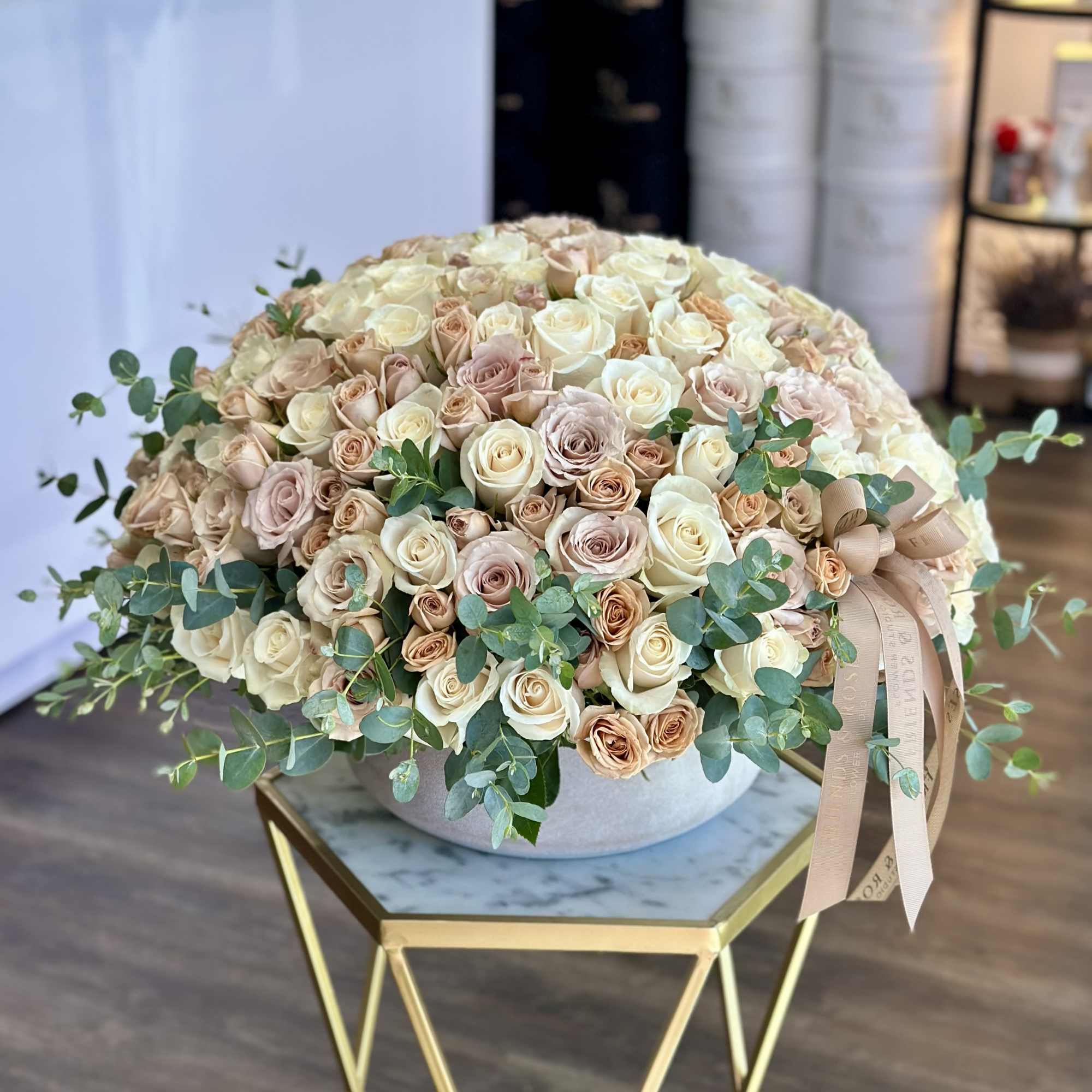Large bouquet of cream and blush roses in a round vase with ribbon.