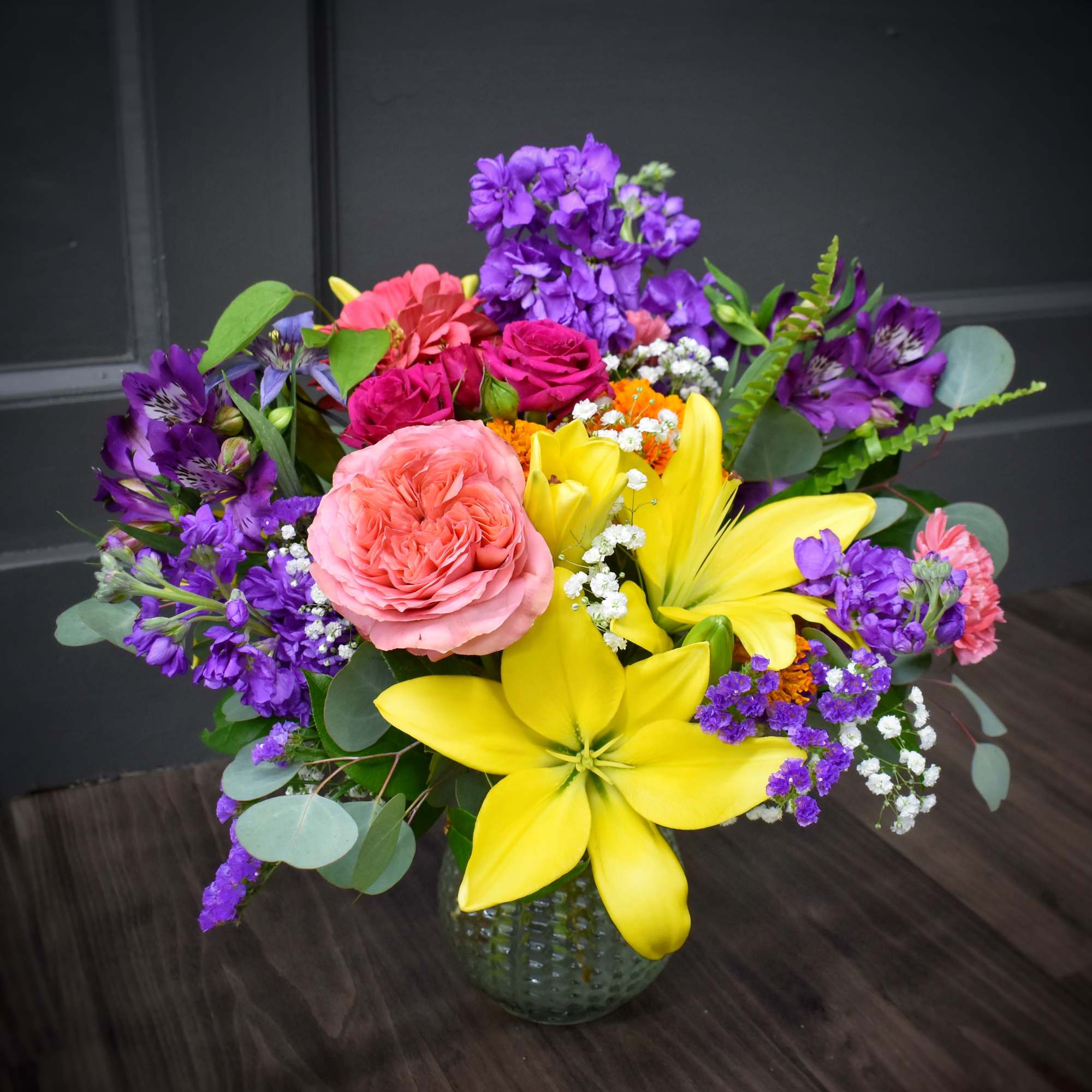 Mixed bouquet with pink roses, yellow lilies, and purple flowers in a glass vase