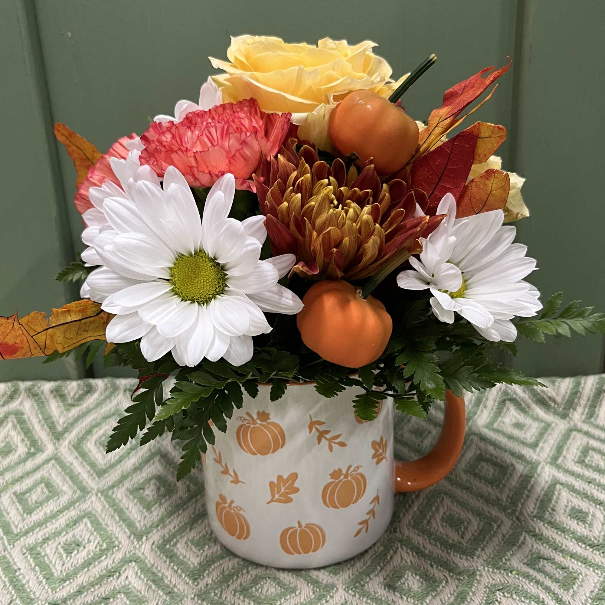 Fall flower arrangement in a pumpkin-decorated mug with daisies and roses