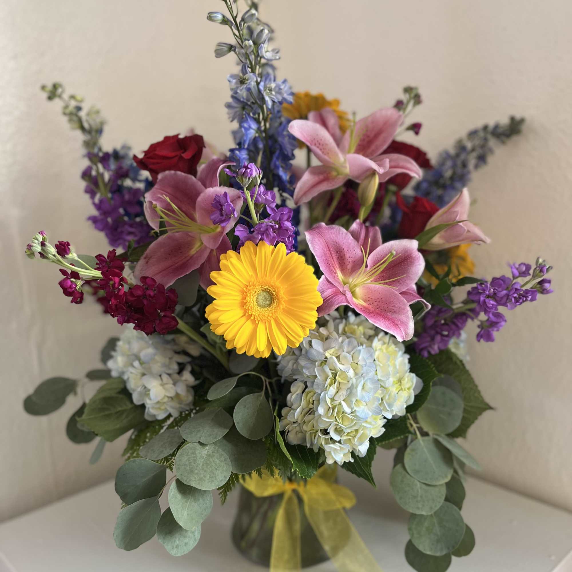 Mixed bouquet with pink lilies, yellow gerbera daisy, hydrangeas, and purple flowers in a vase