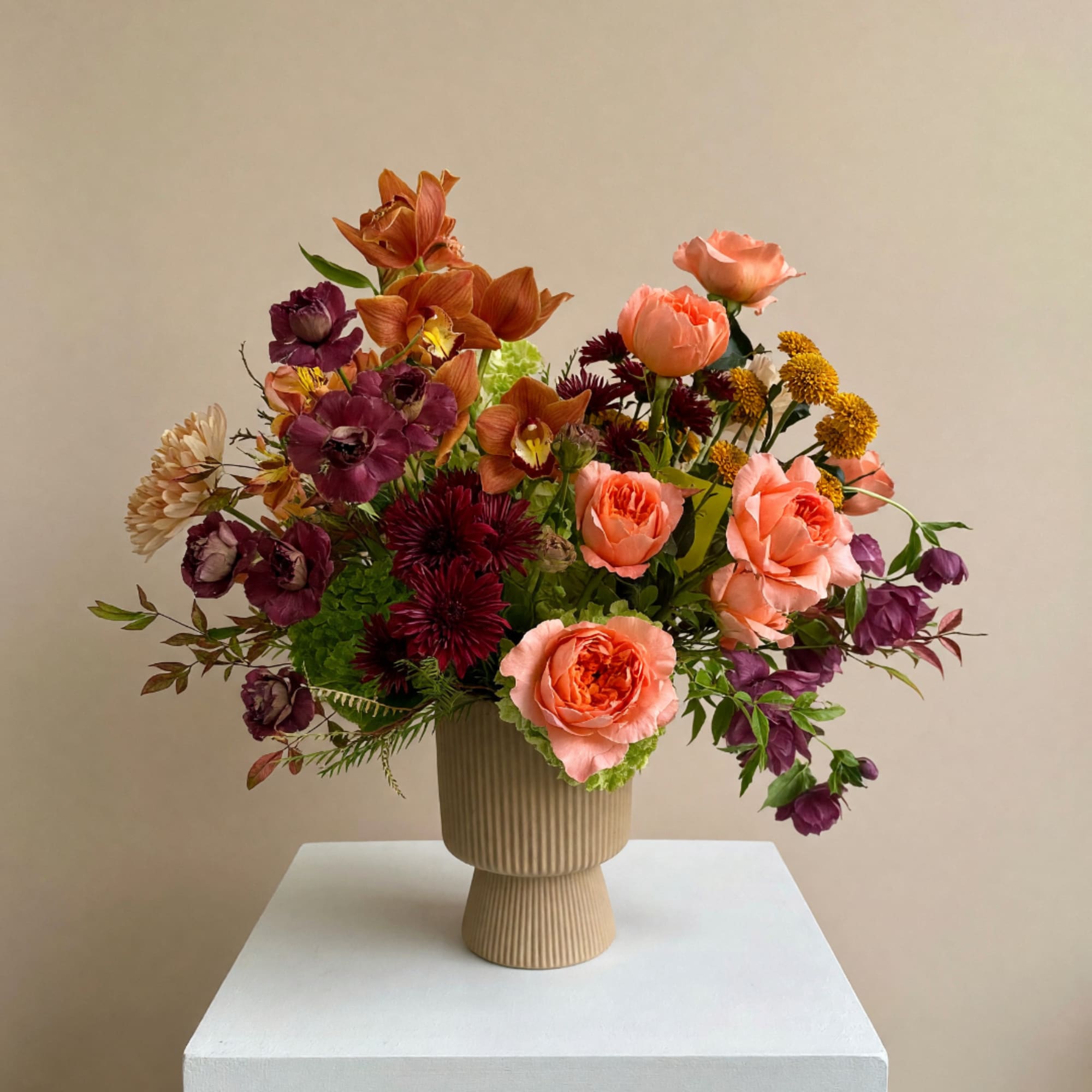Mixed bouquet of peach, purple, and yellow flowers in a ribbed beige vase