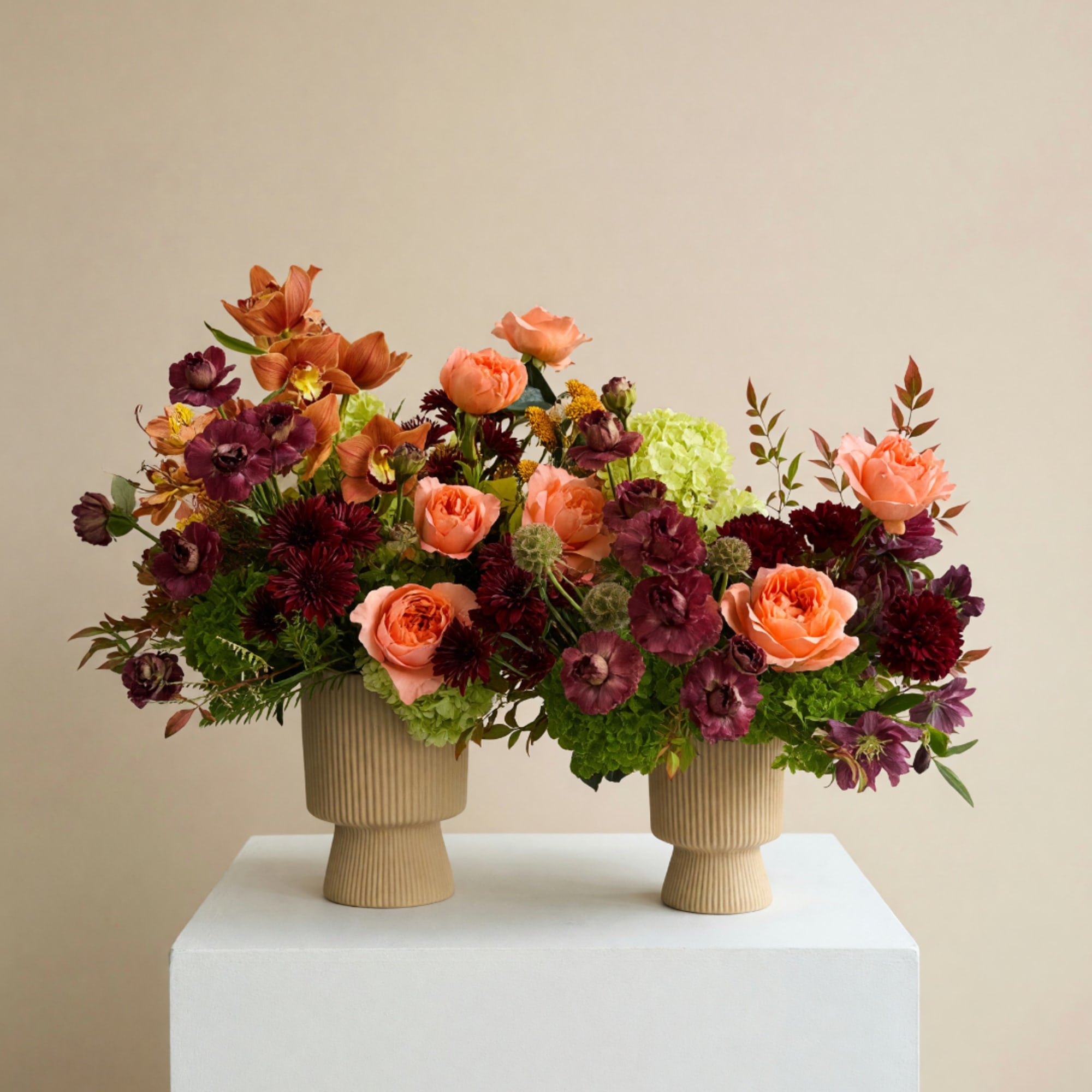Two floral arrangements in ribbed beige vases with peach and burgundy blooms