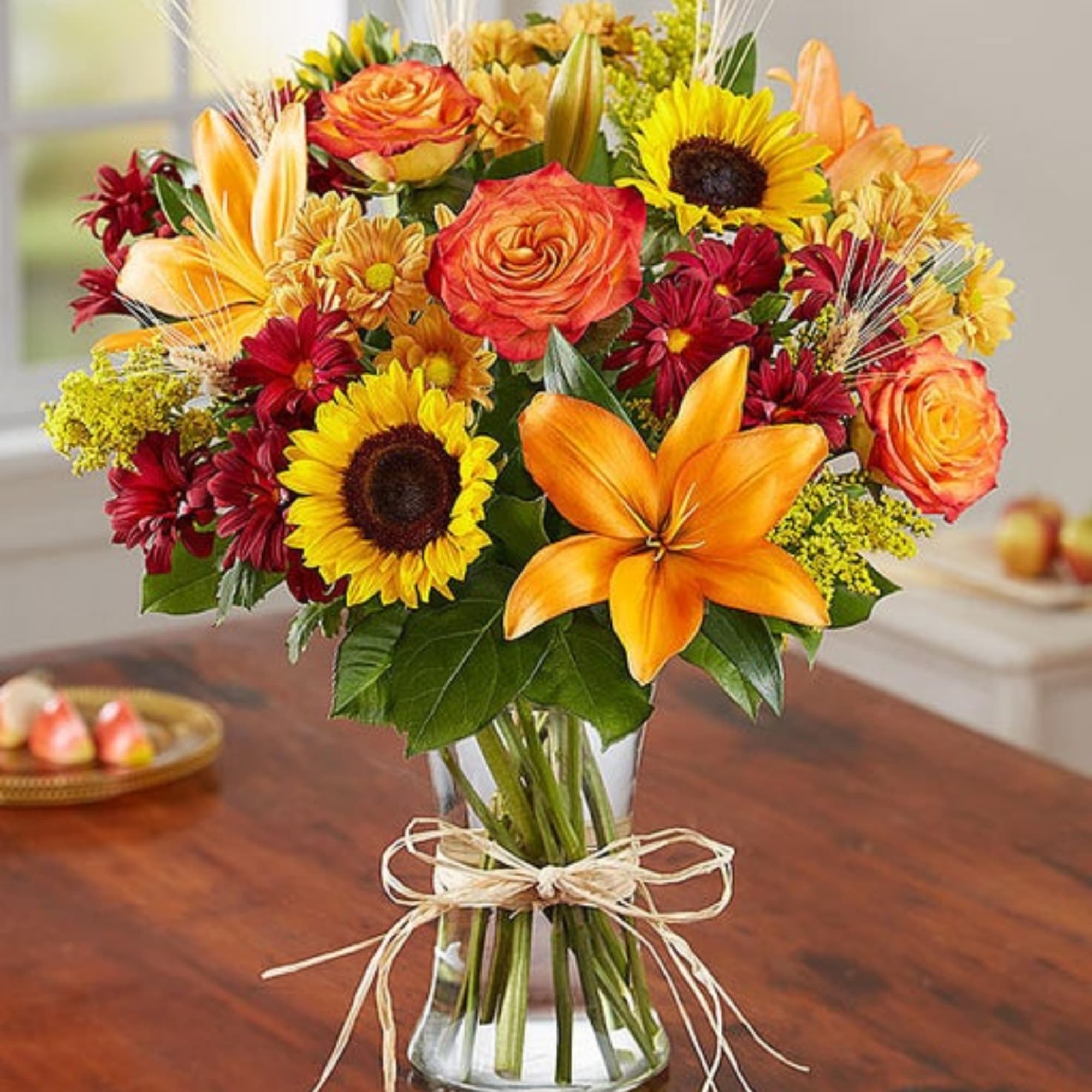Bouquet of sunflowers, orange roses, lilies, and red daisies in a glass vase