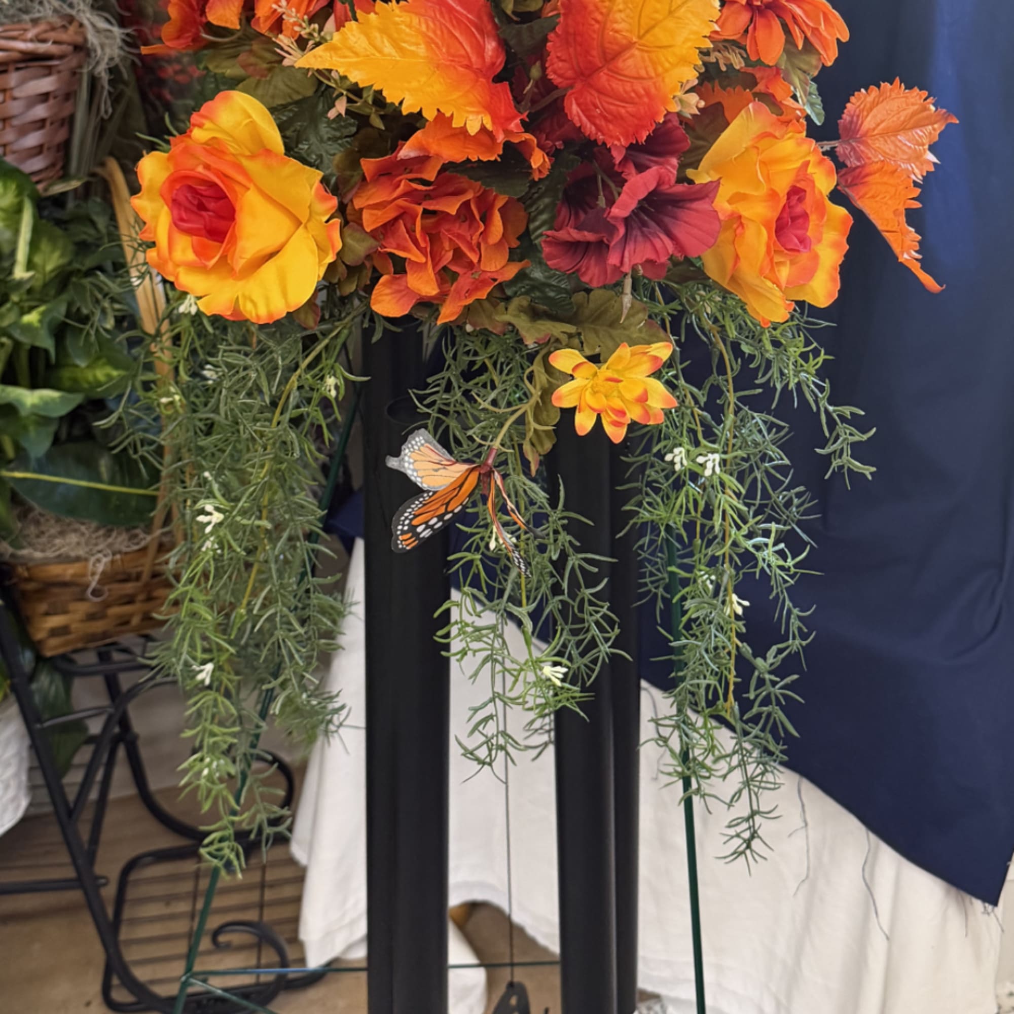 Orange and yellow floral arrangement with trailing greenery on a stand