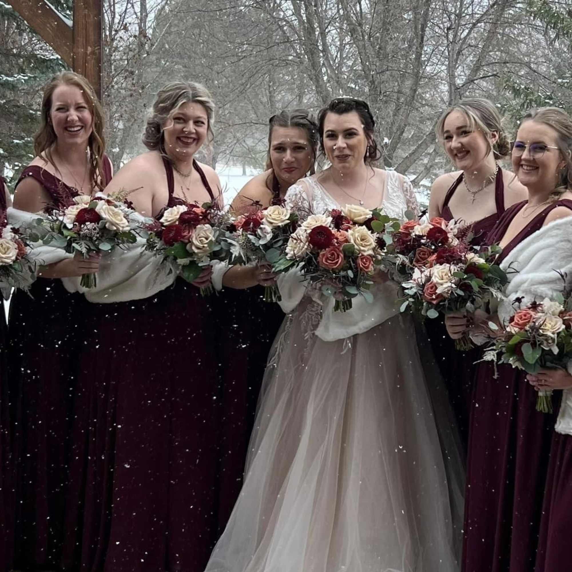 Bridal party holding burgundy and cream bouquets in the snow