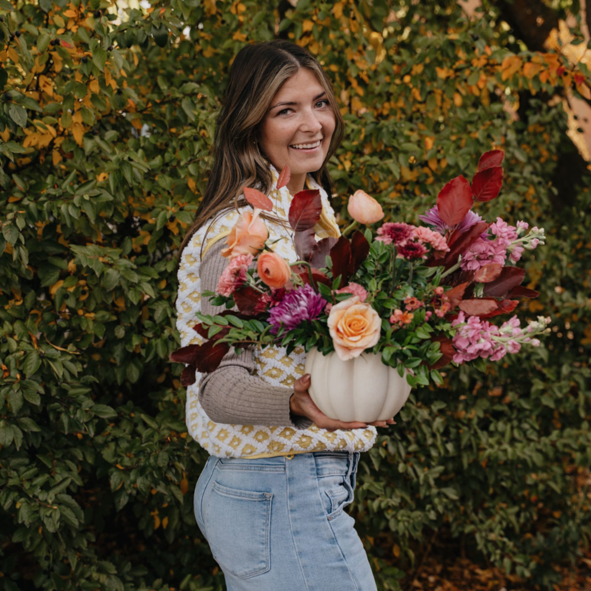 Woman holding a white pumpkin vase filled with pink and peach flowers