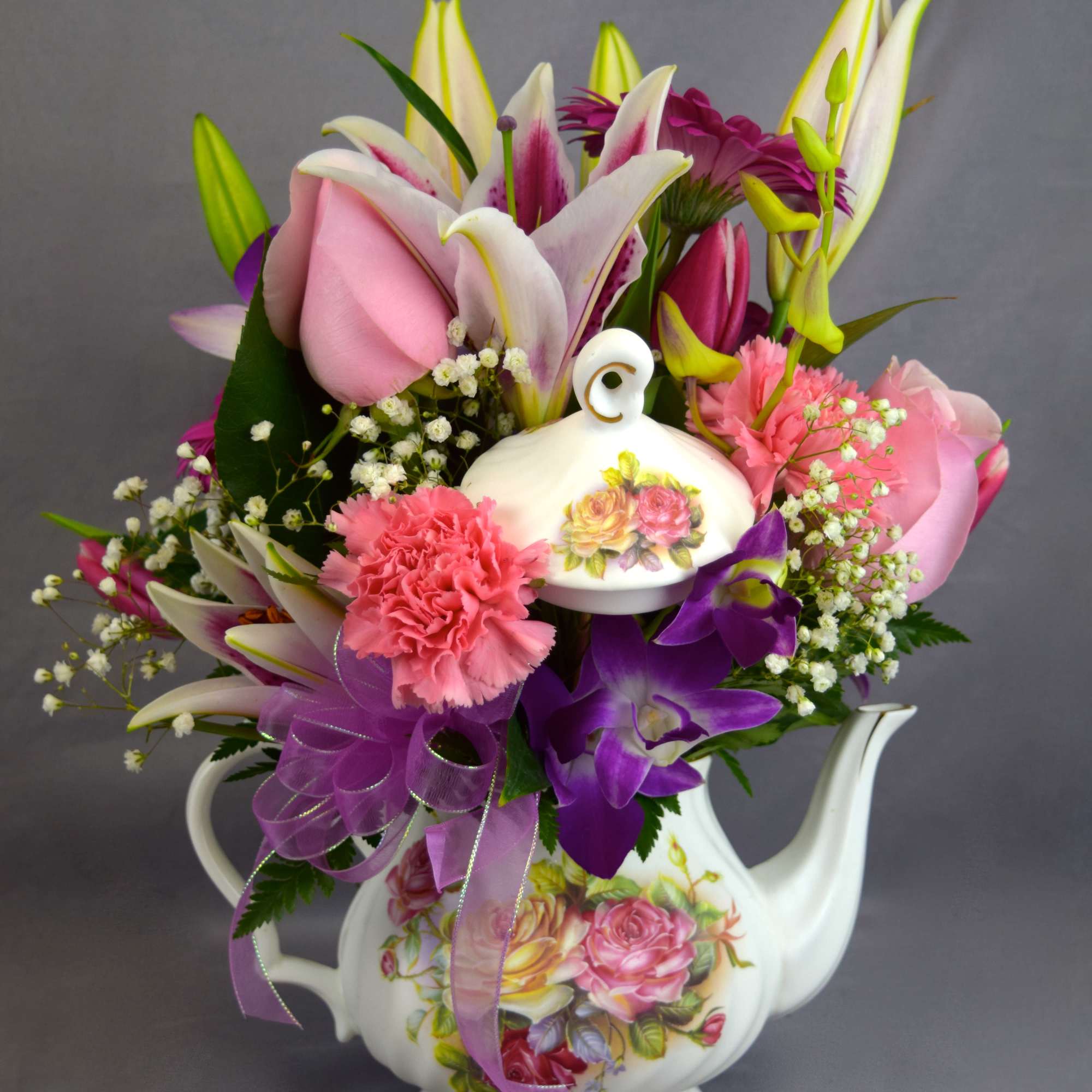 Pink and purple flowers arranged in a white teapot vase