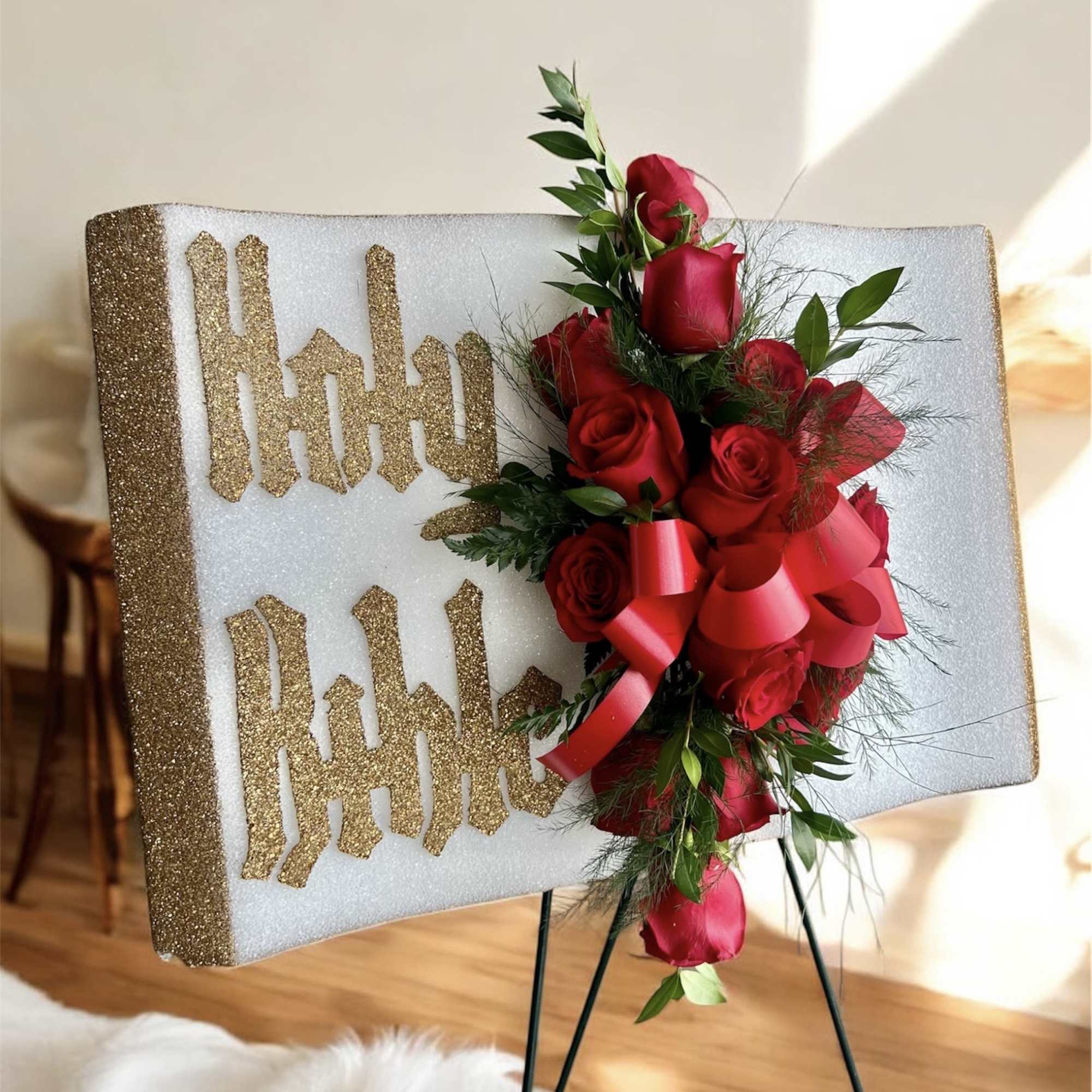 Red rose arrangement on a glittery display board with gold lettering