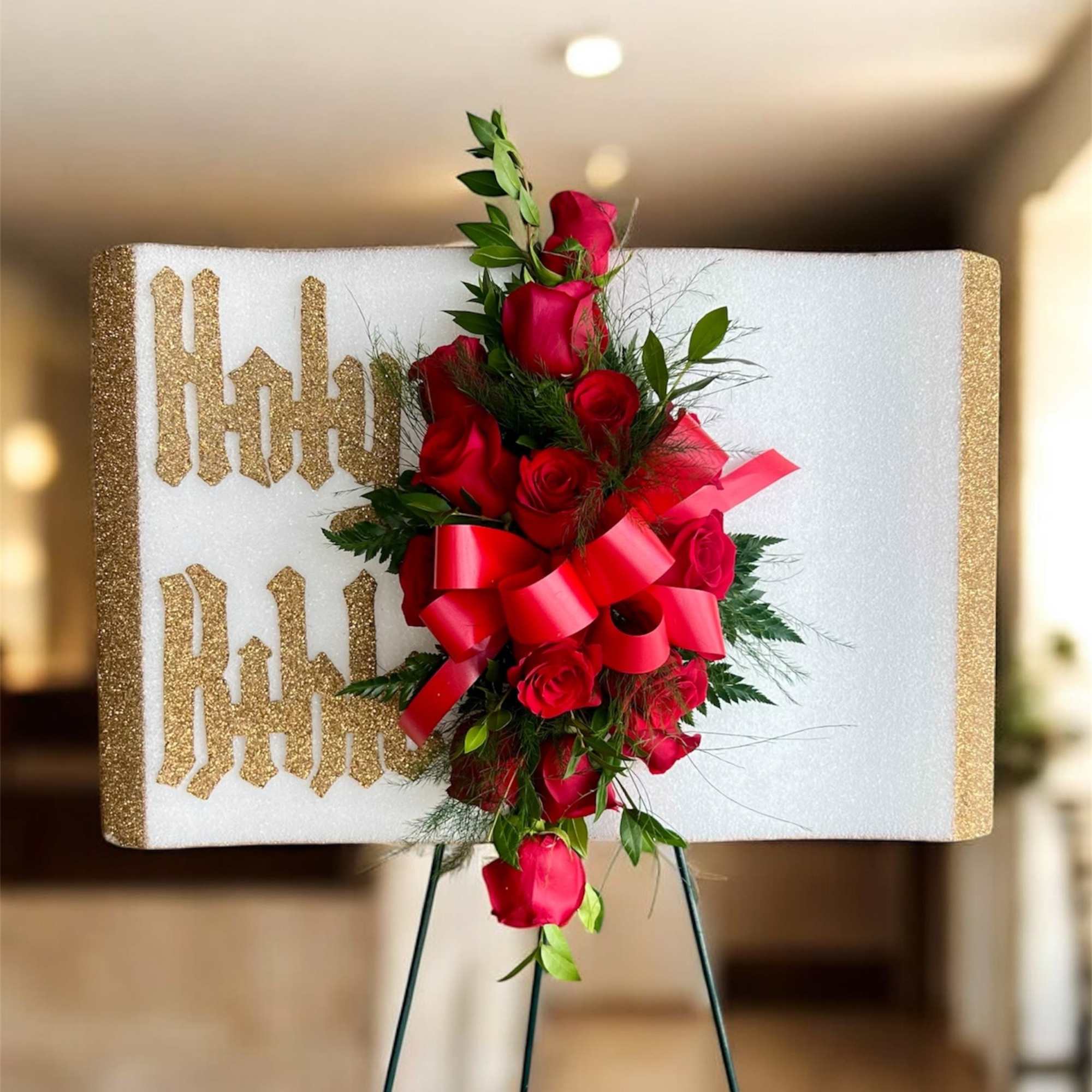 Red rose arrangement on a glittery white display board with a red ribbon