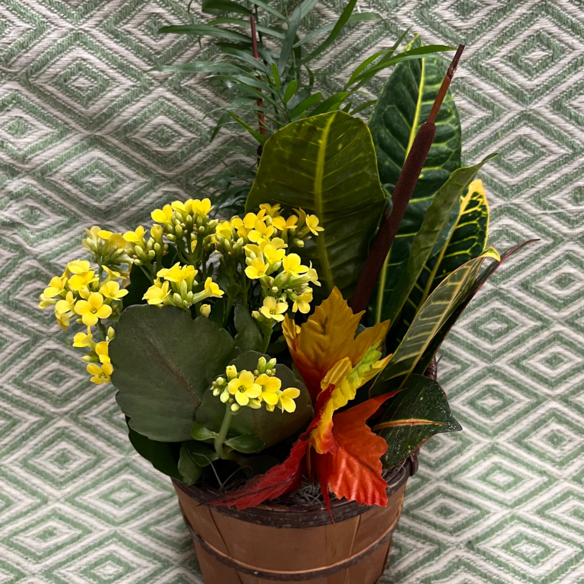 Potted arrangement with yellow flowers and broad tropical leaves in a wooden container