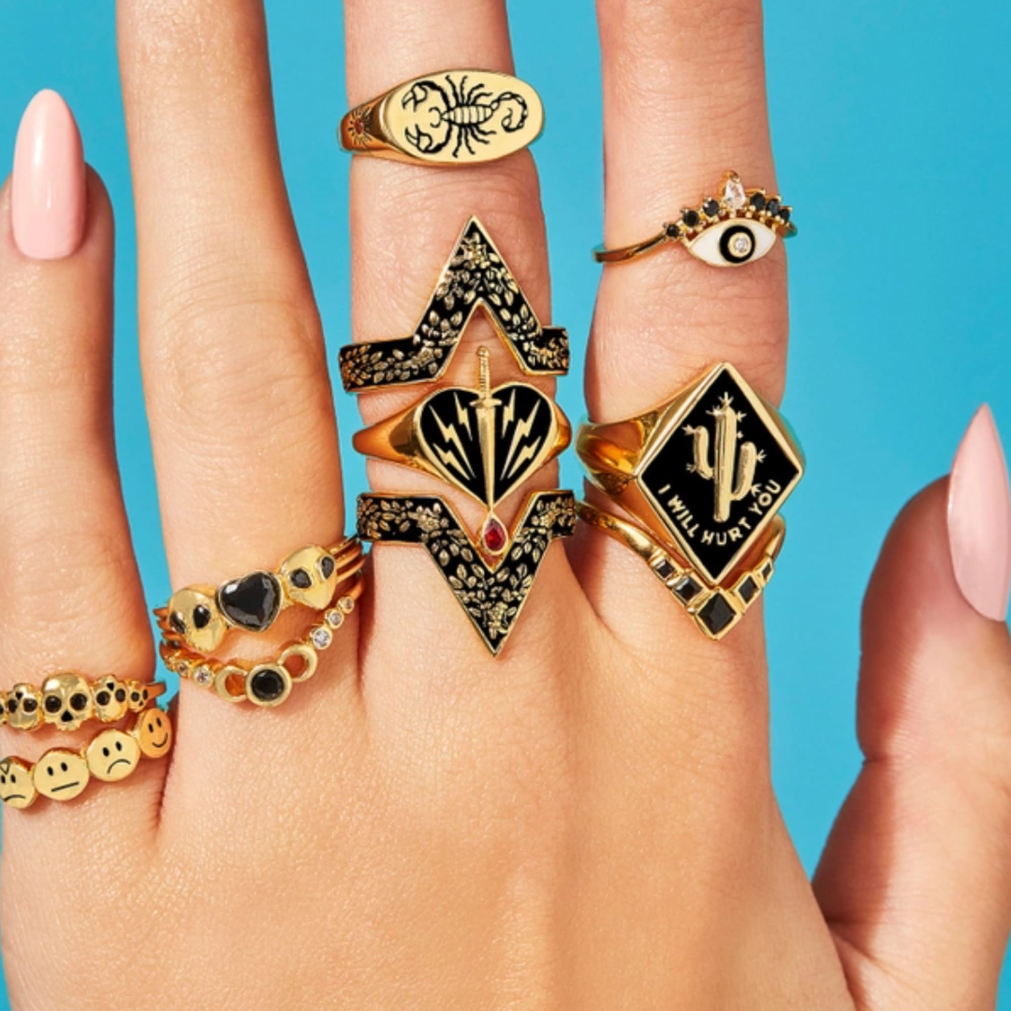 Hands wearing multiple gold rings against a blue background