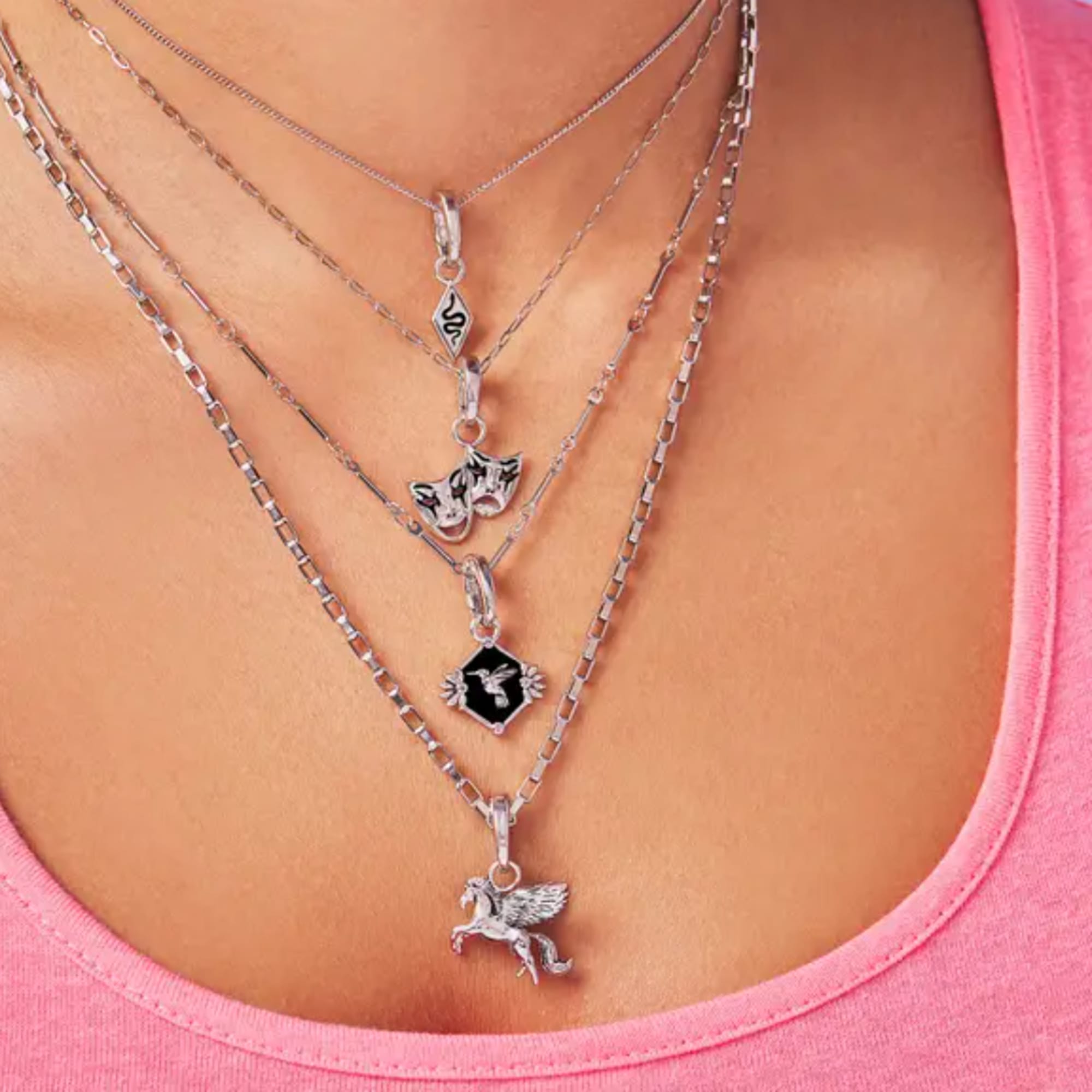 Layered silver necklaces with small pendants worn over a pink top