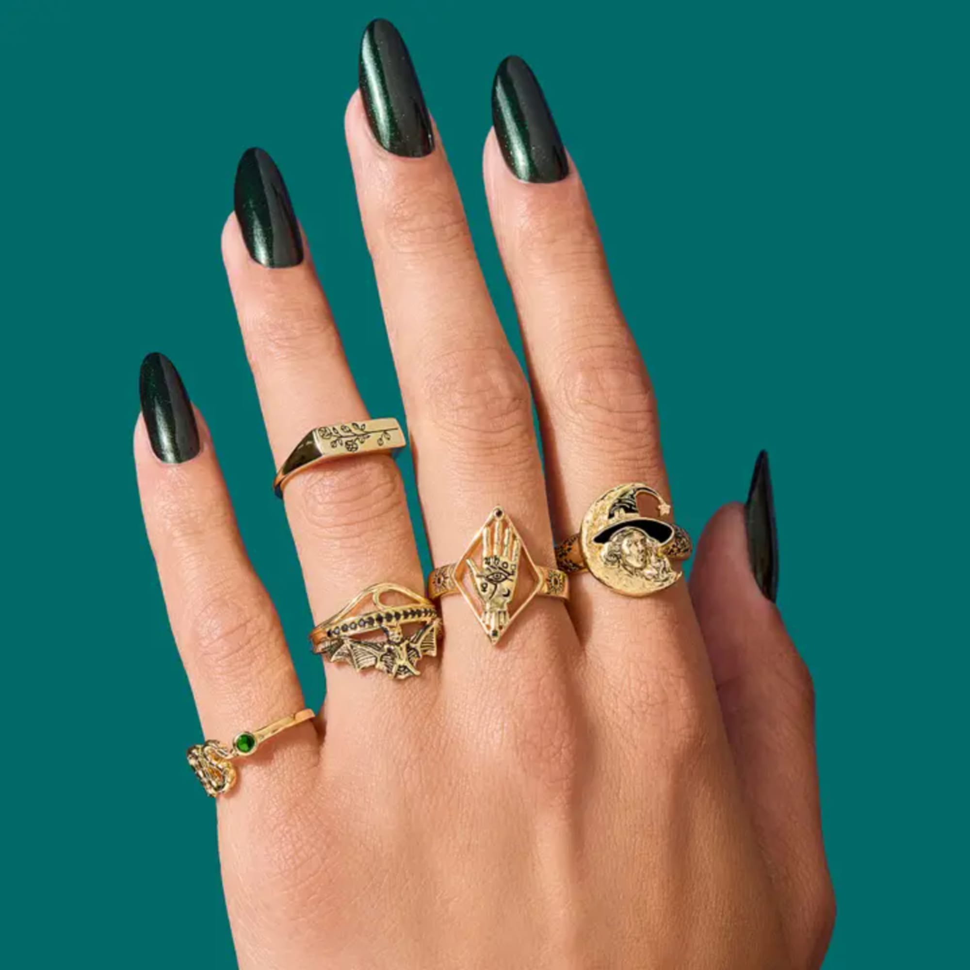 Hand wearing several gold rings with black nails on a teal background