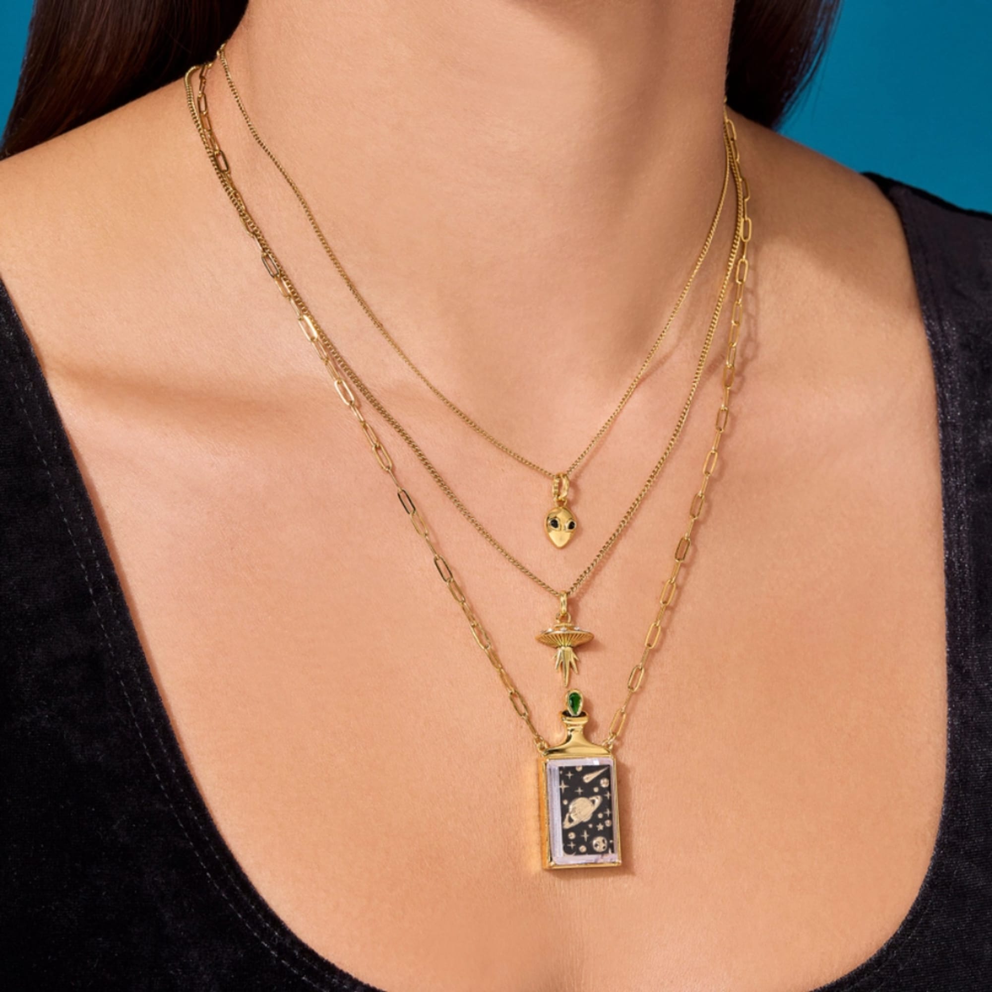 Layered gold necklaces with small pendants worn on a person’s neck