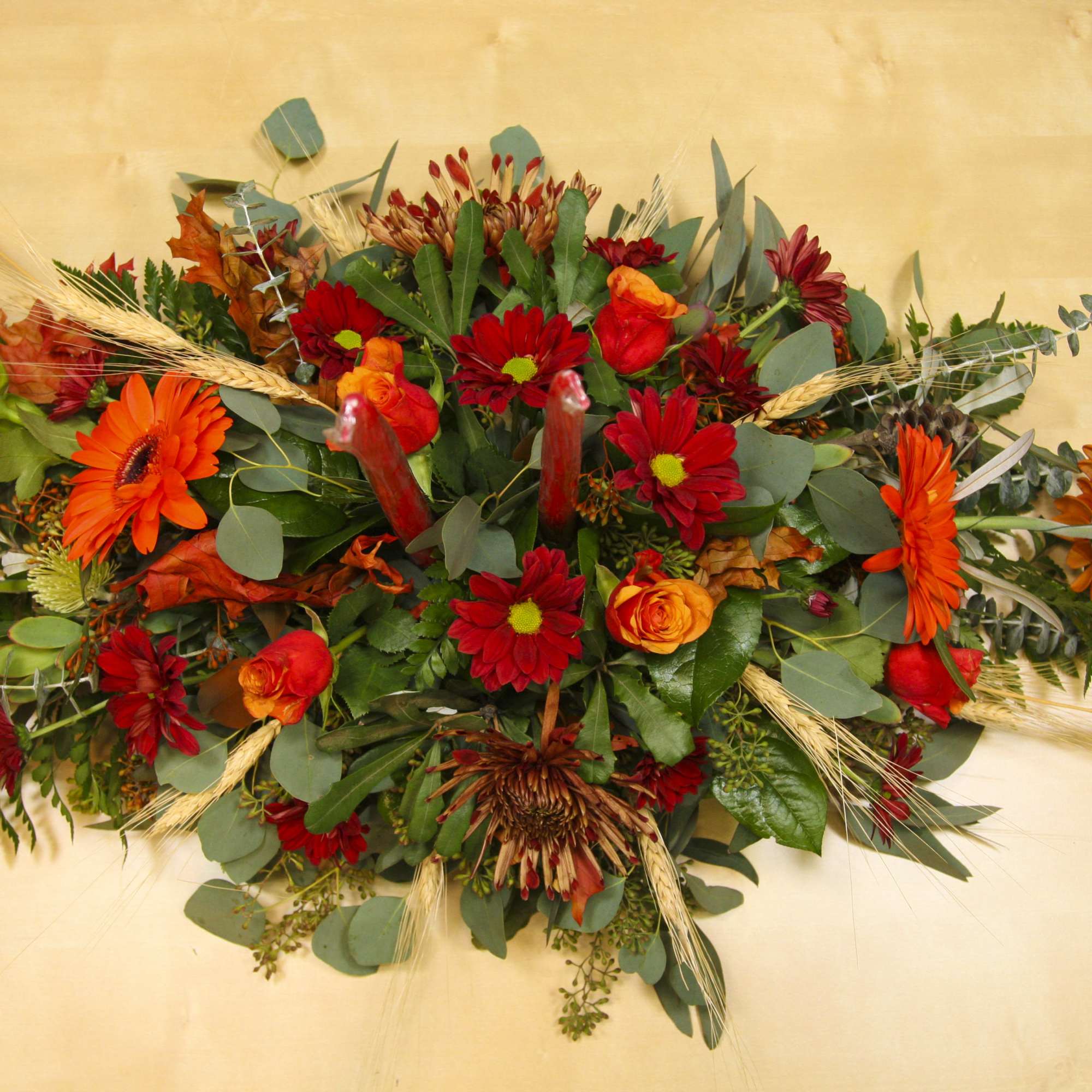 Autumn floral arrangement with red and orange flowers on a tan background