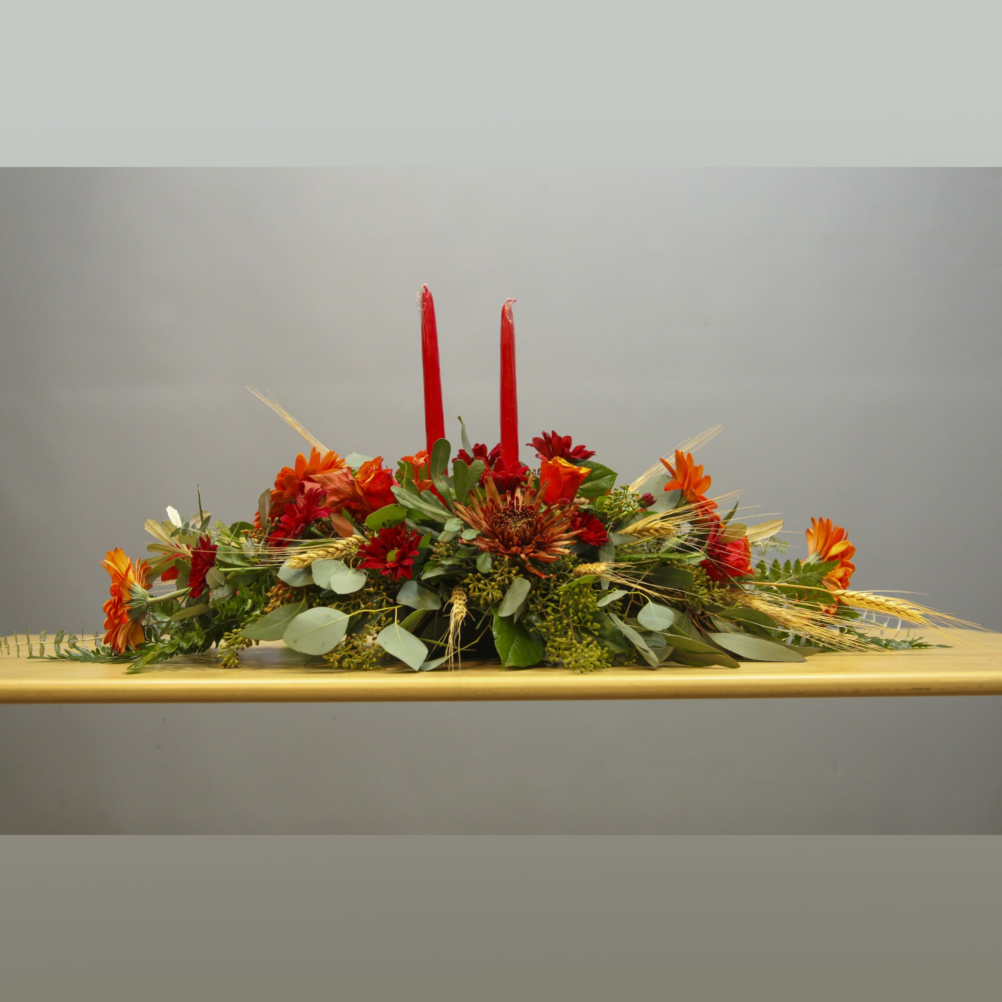 Low floral centerpiece with red candles and orange-red flowers