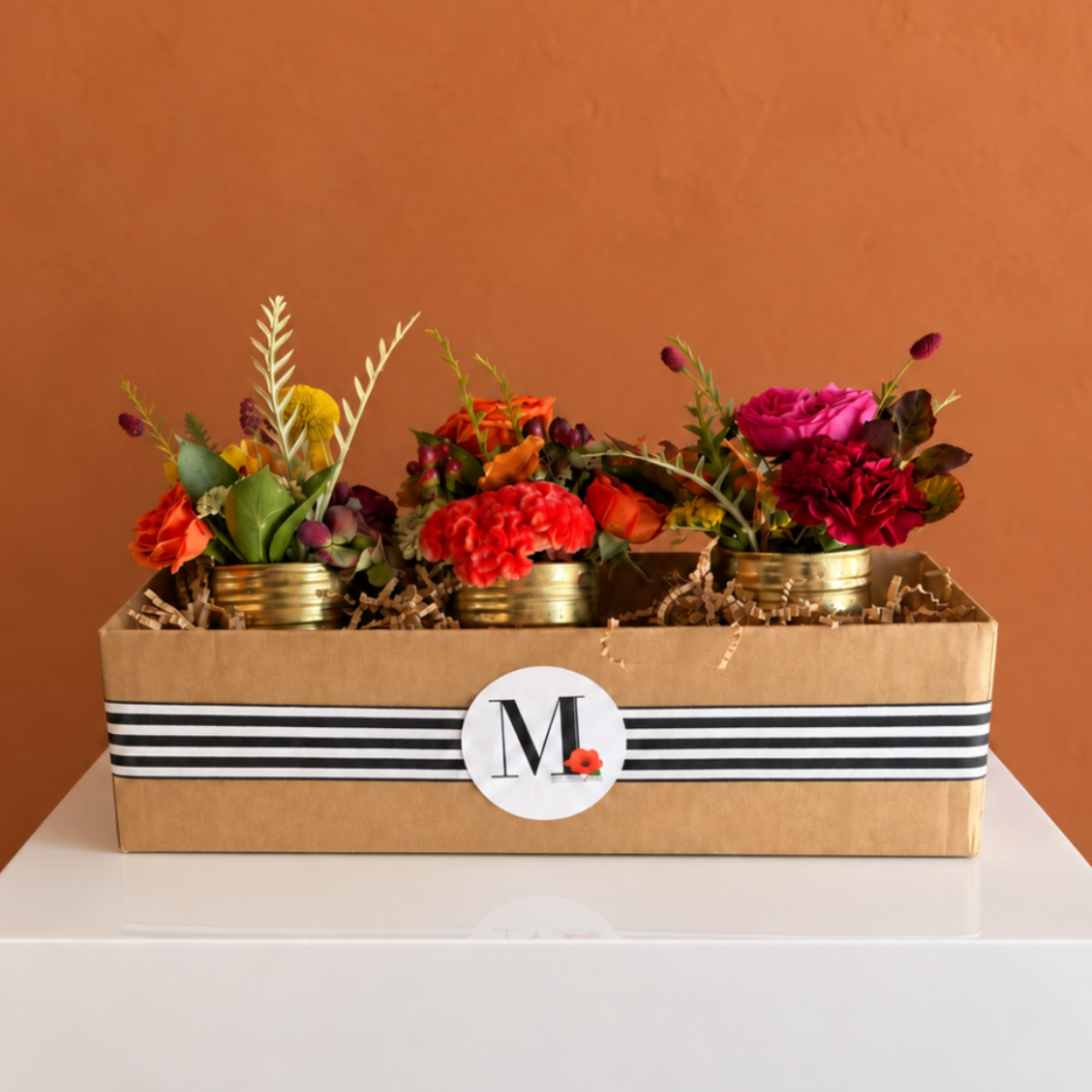 Three small floral arrangements in gold tins inside a gift box