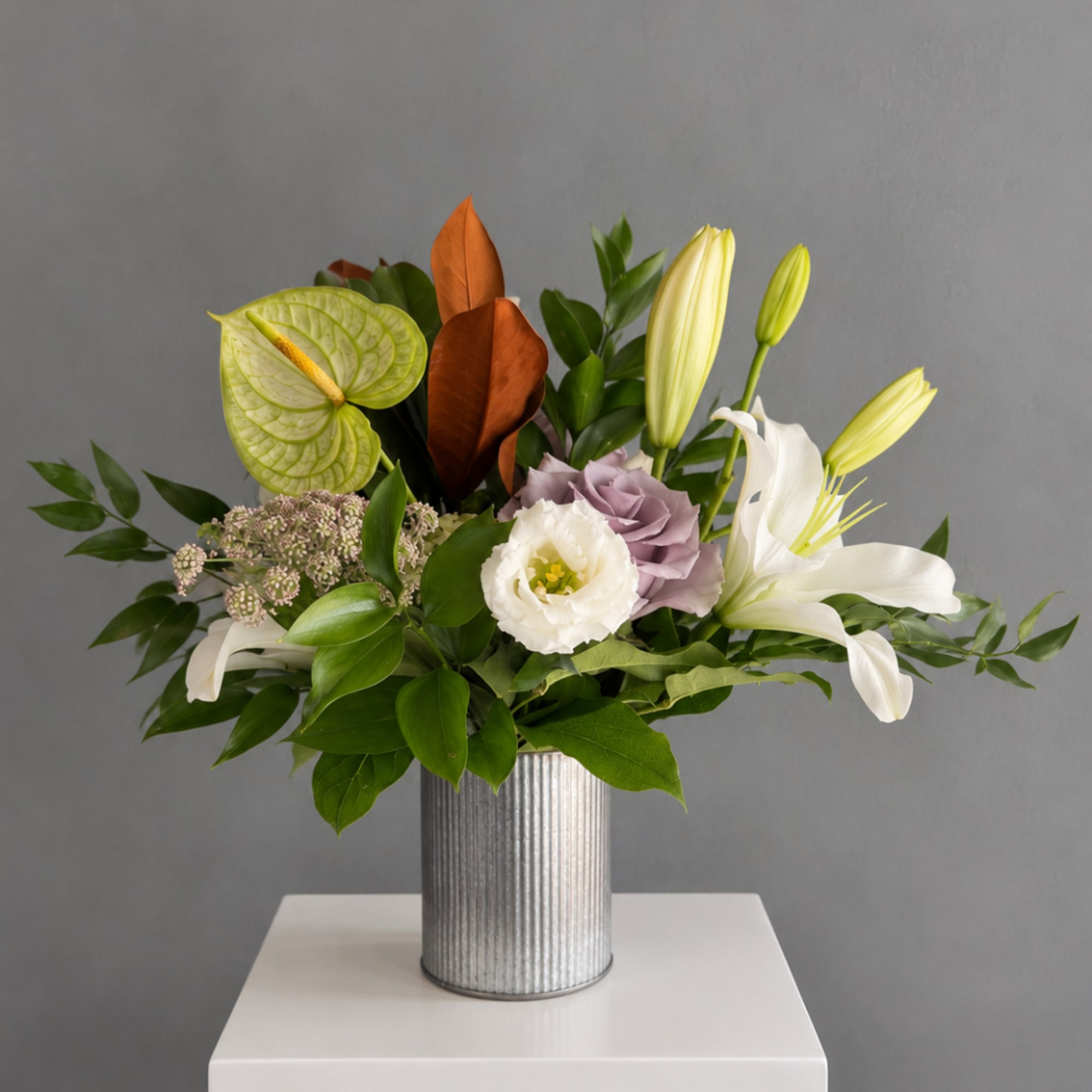 Mixed floral arrangement in a ribbed silver vase with white lilies and pale blooms