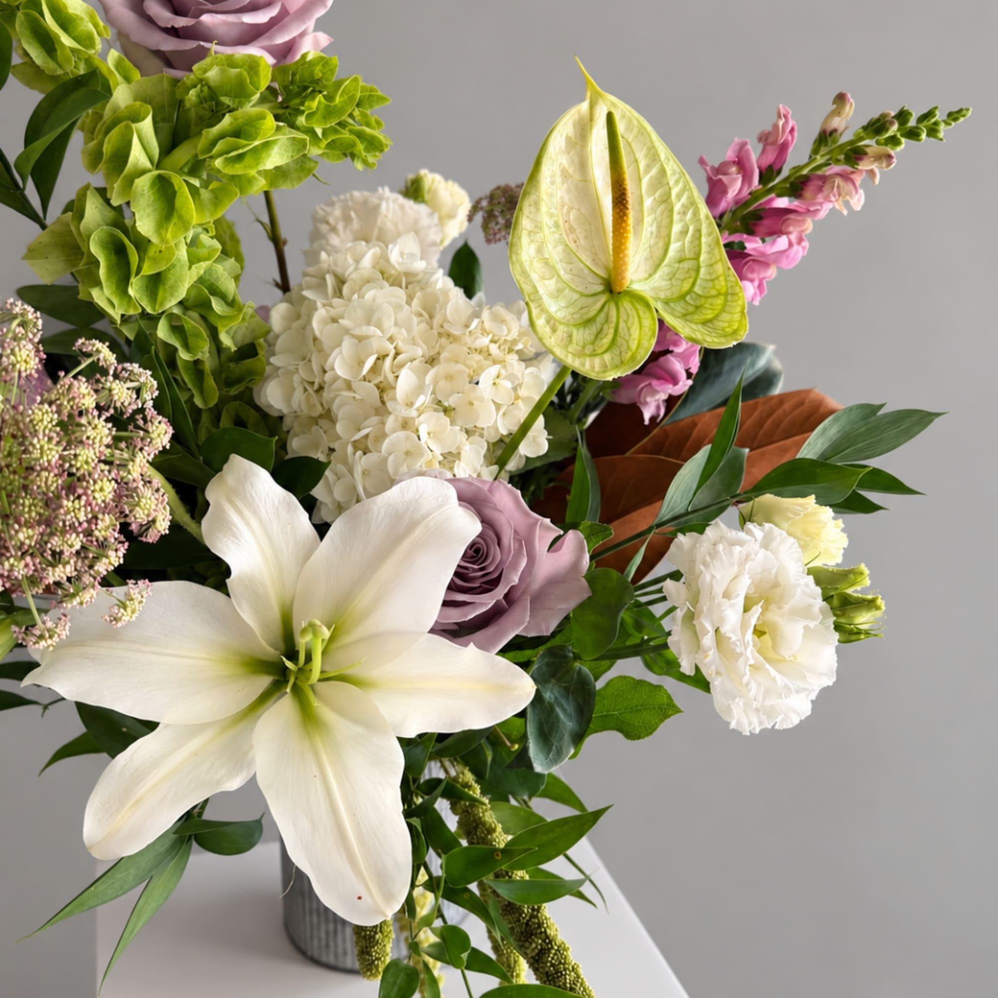 Mixed bouquet with white lilies, hydrangea, roses, and pink blooms in a vase