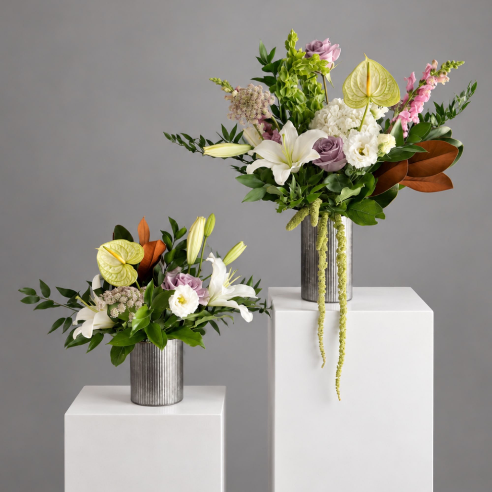 Two floral arrangements in ribbed metal vases on white pedestals