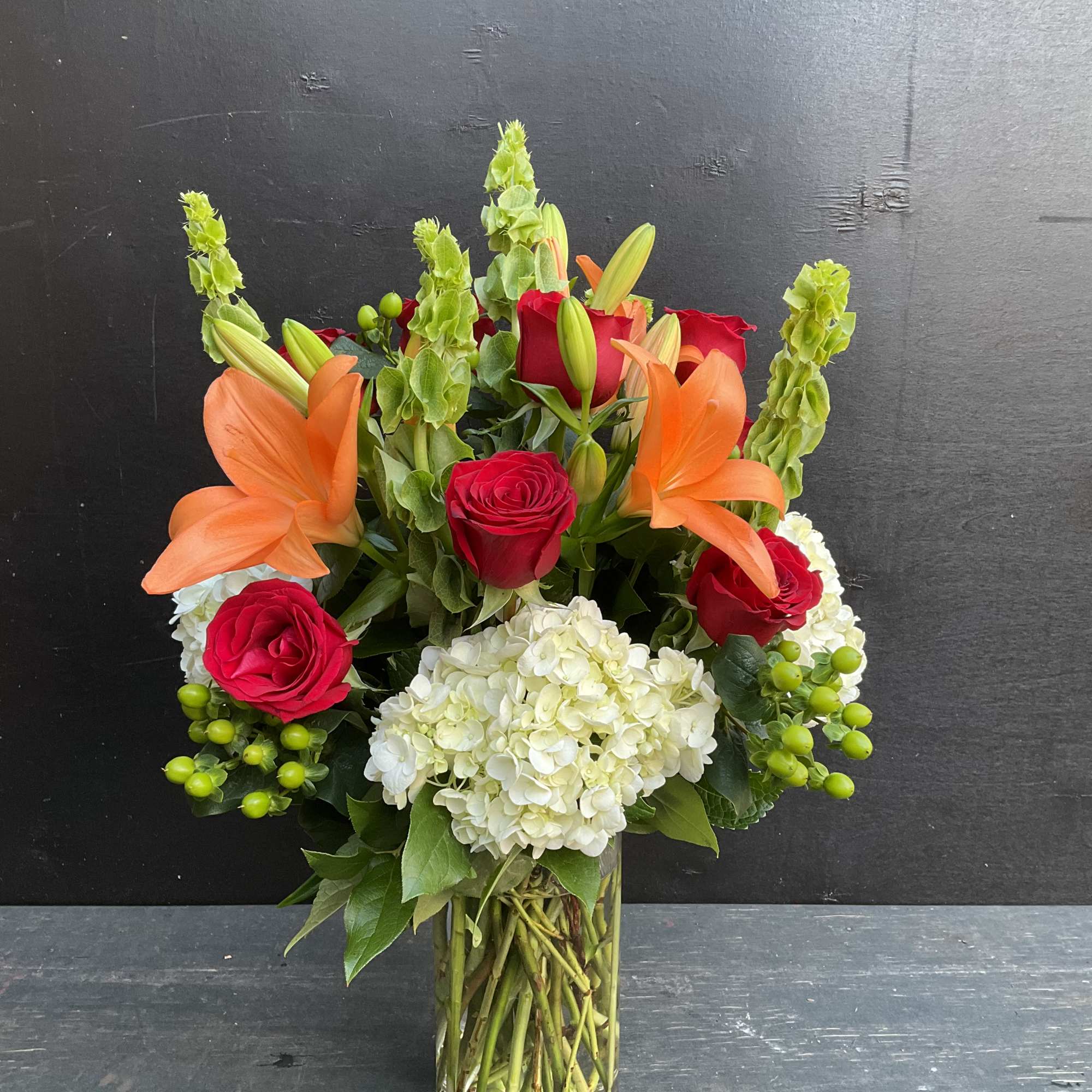 Bouquet of red roses, orange lilies, and white hydrangea in a glass vase
