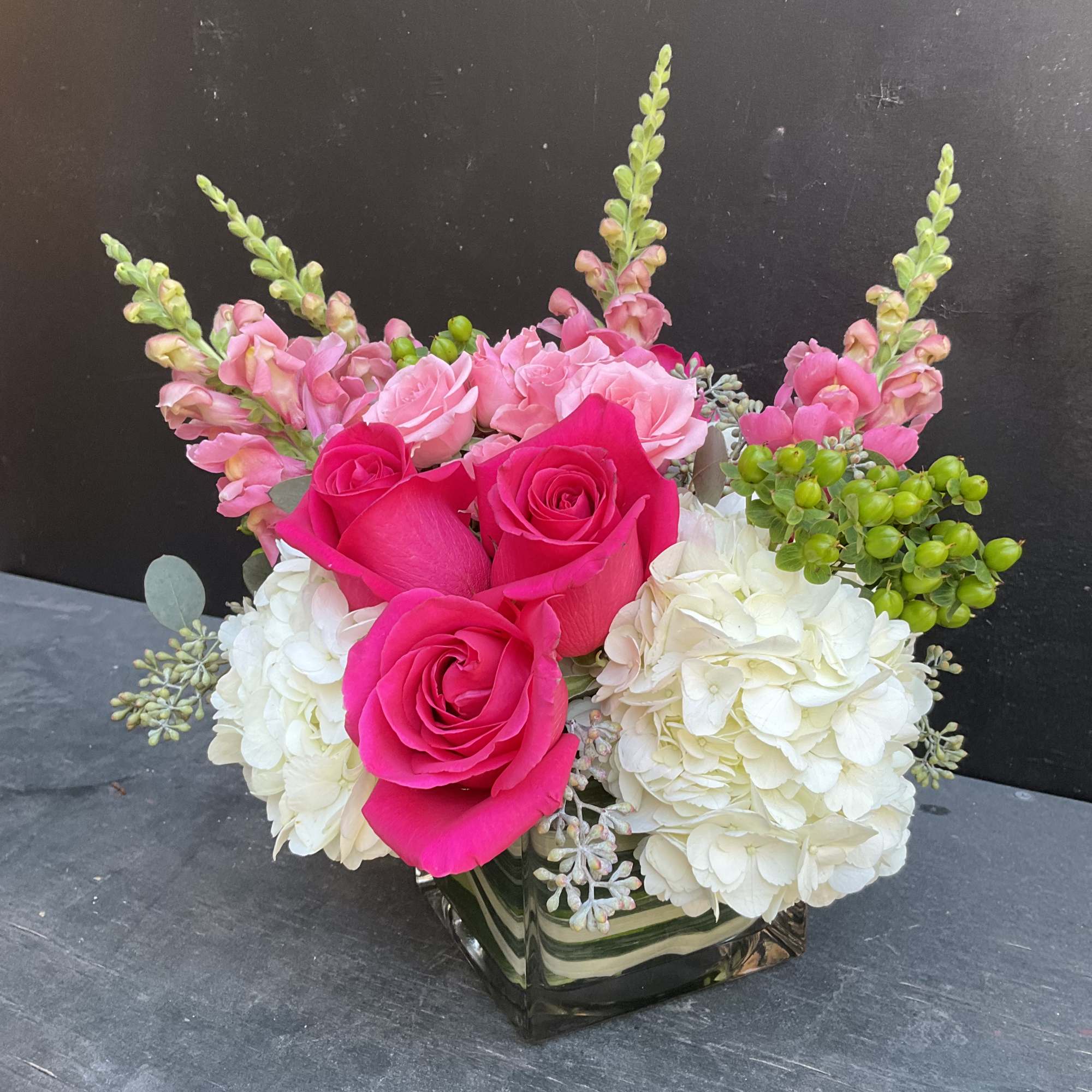 Pink roses and white hydrangeas arranged in a square glass vase