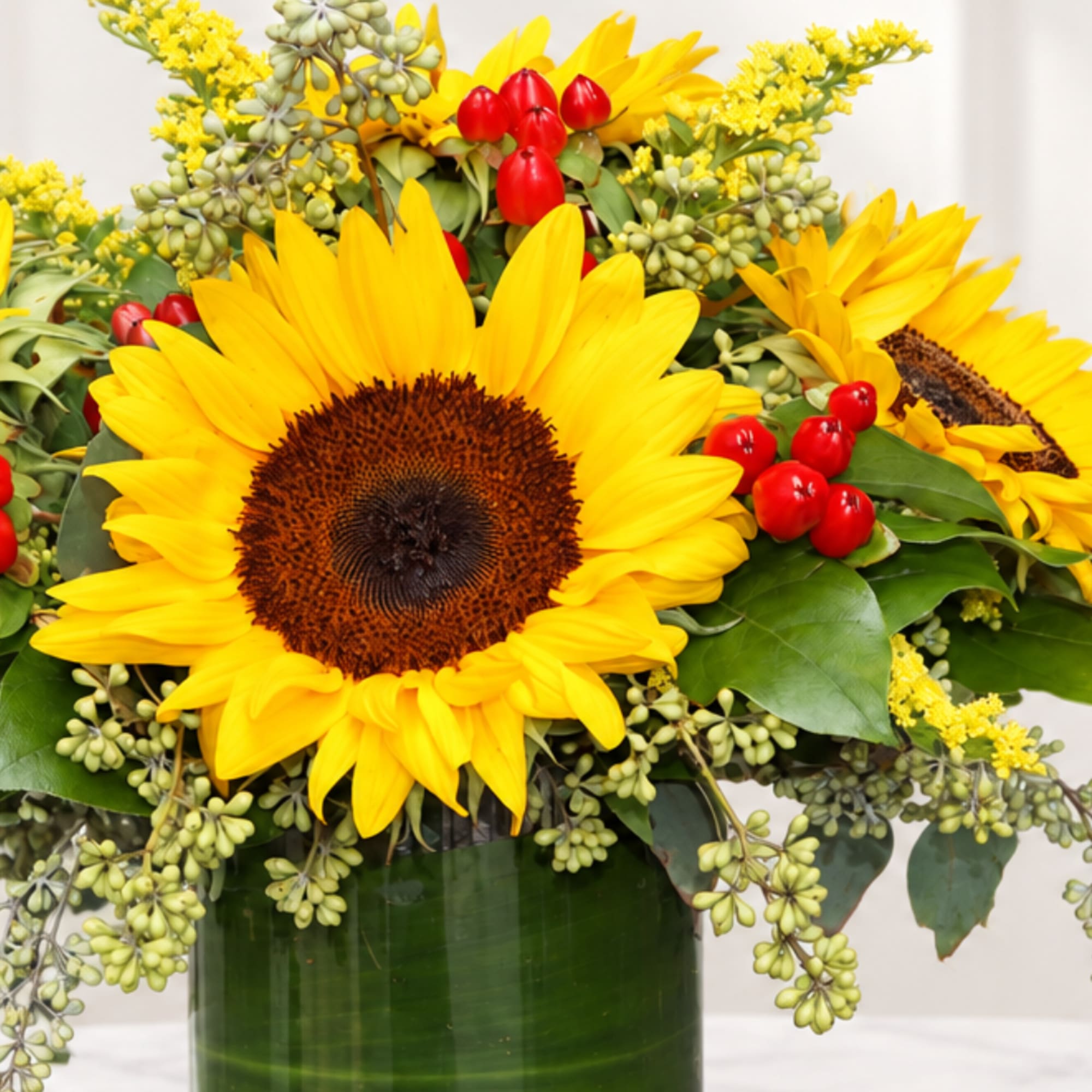 Sunflower arrangement in a green vase with red berry accents
