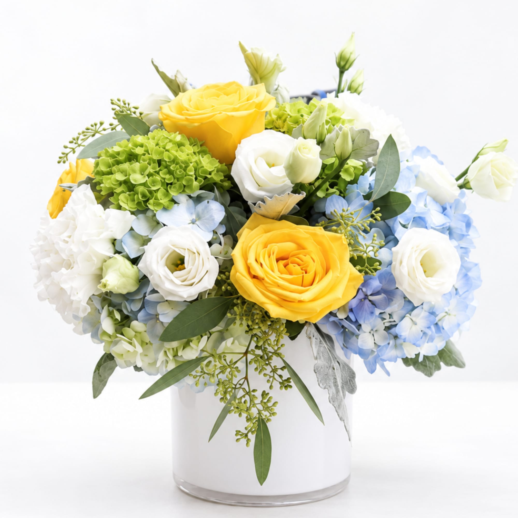 Yellow and white roses with blue hydrangeas in a clear vase