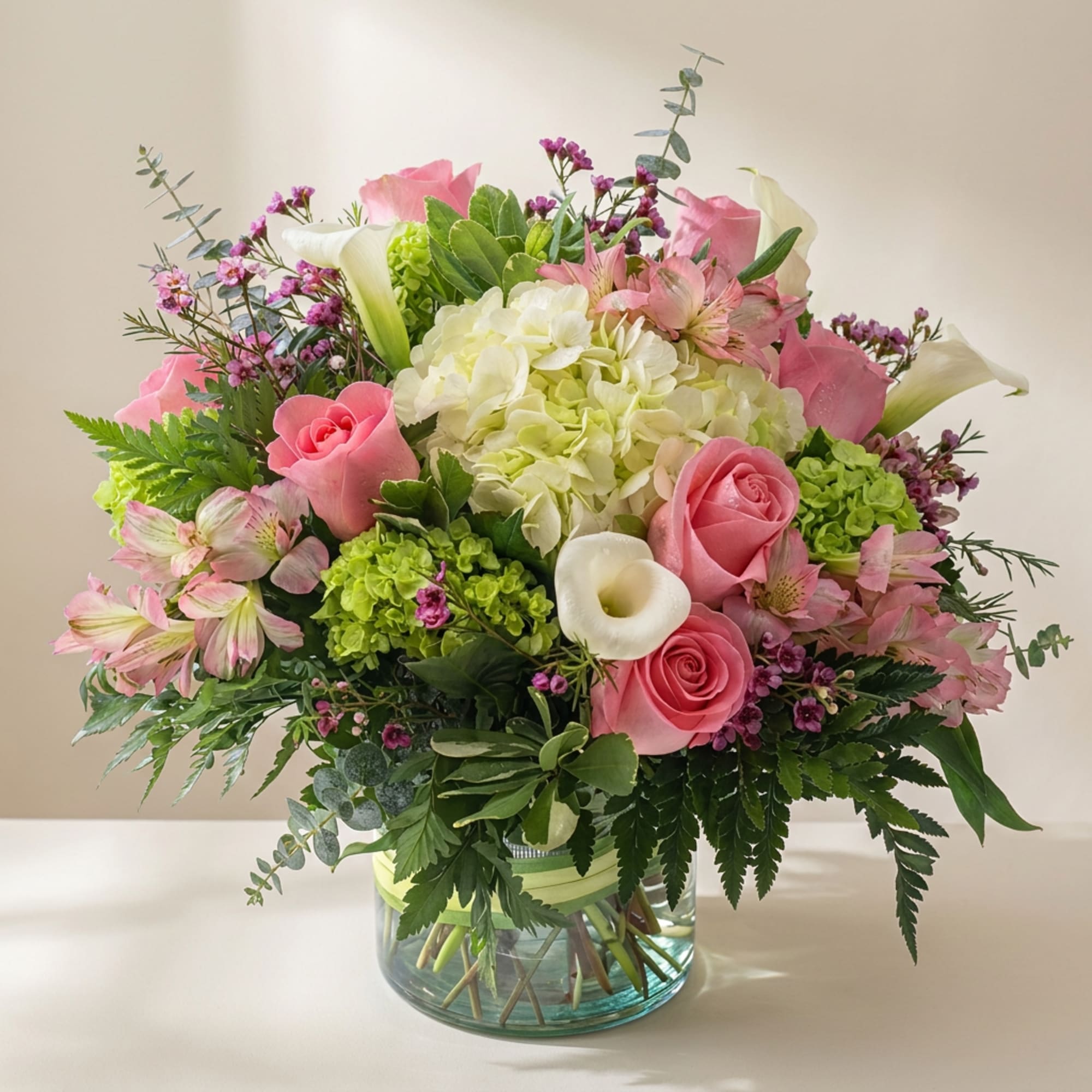 Pink roses, white calla lilies, and hydrangeas in a glass vase