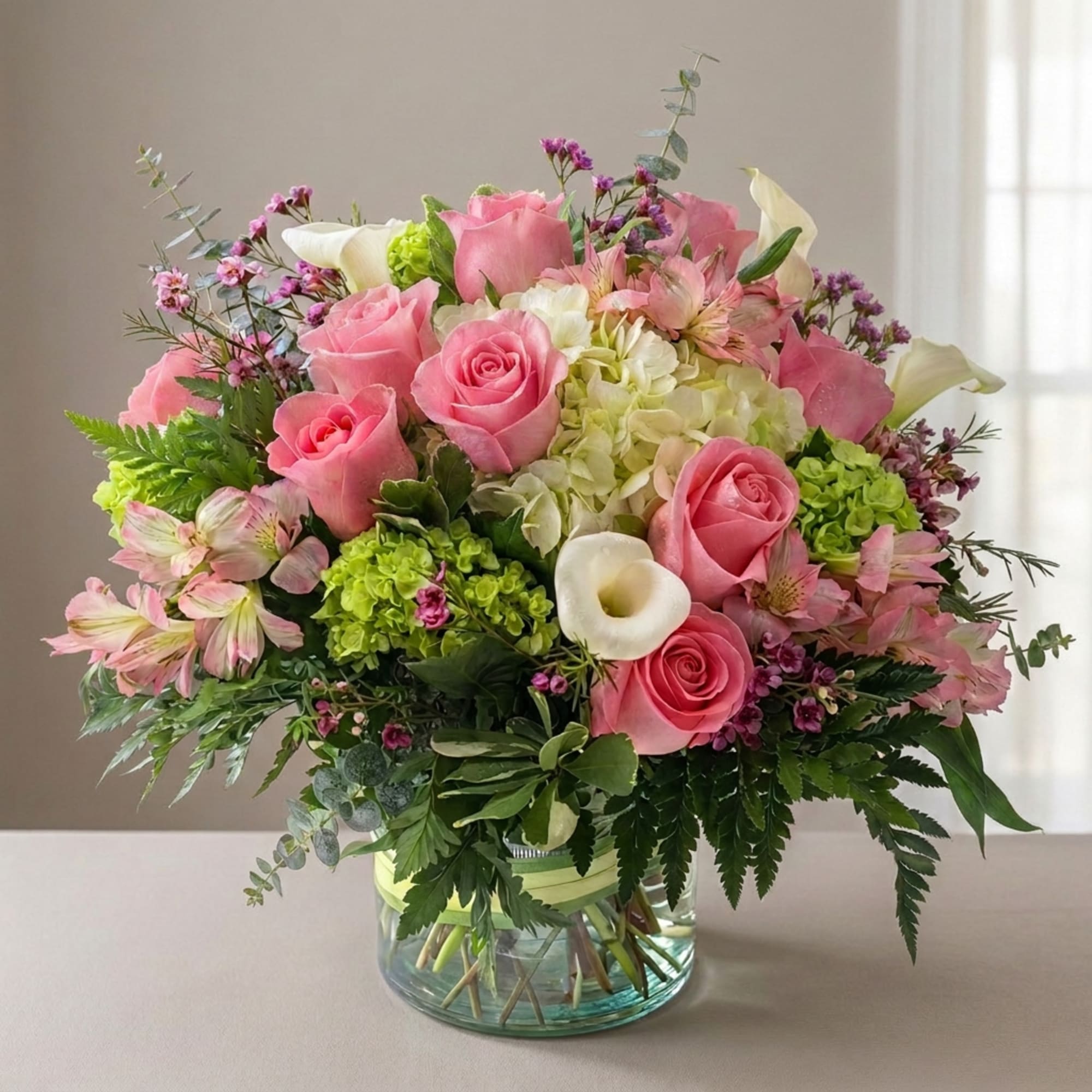 Pink roses and white calla lilies in a glass vase with mixed blooms