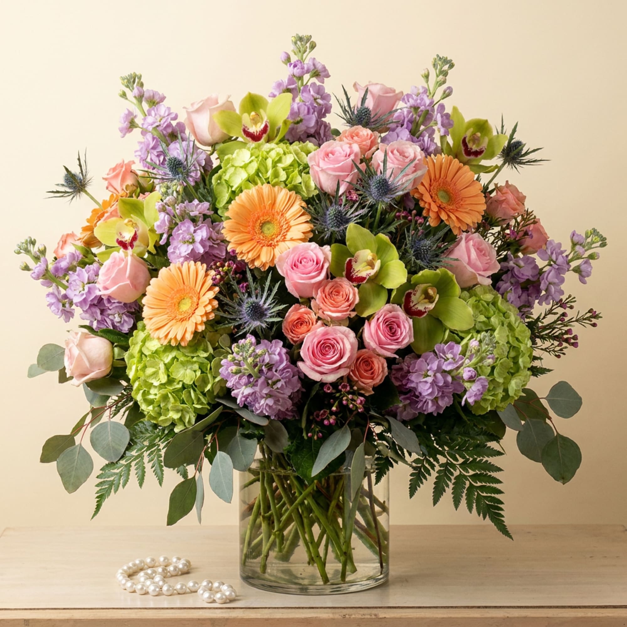 Mixed bouquet of pink roses, orange gerberas, and purple blooms in a glass vase