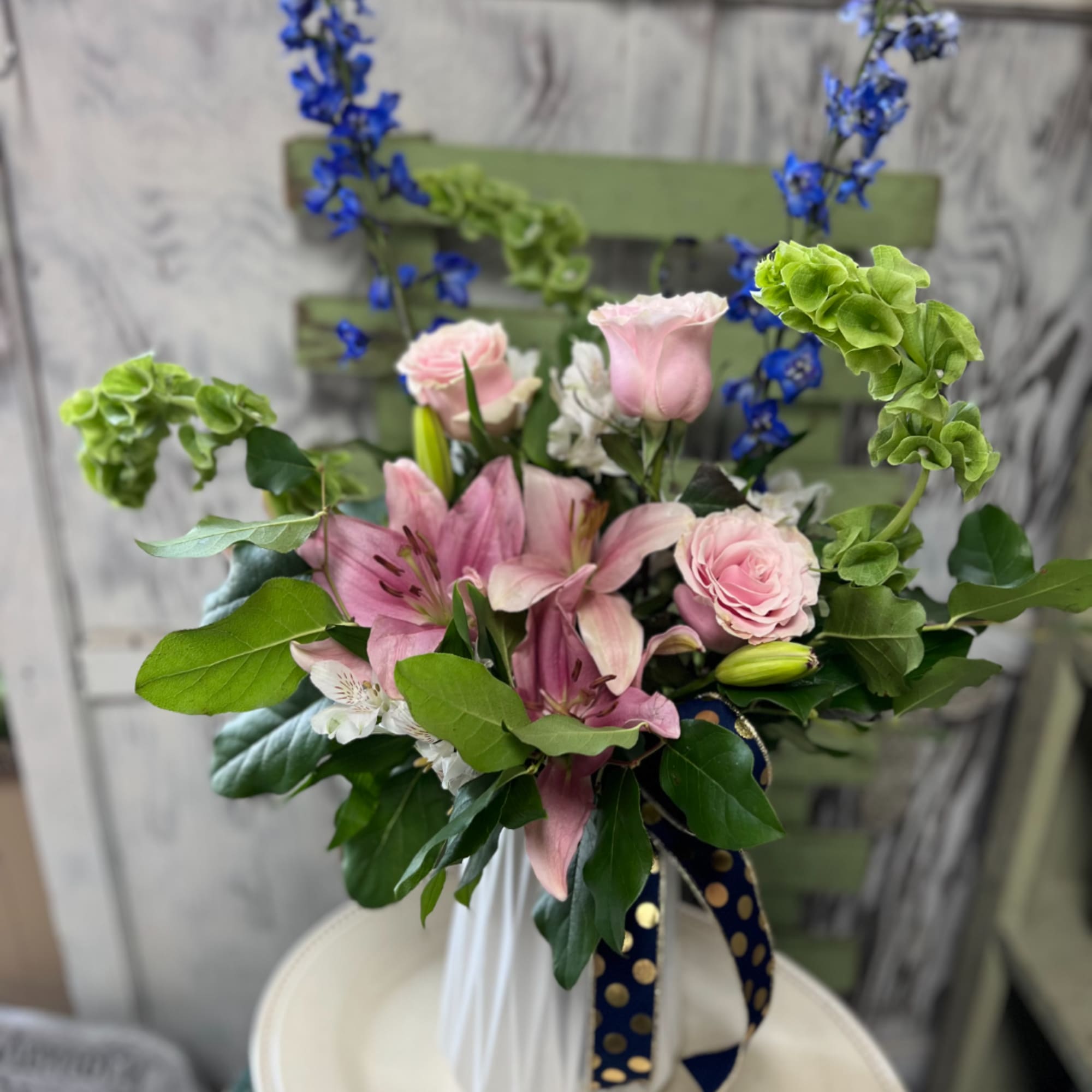 Pink lilies and roses in a white vase with blue flowers and green accents