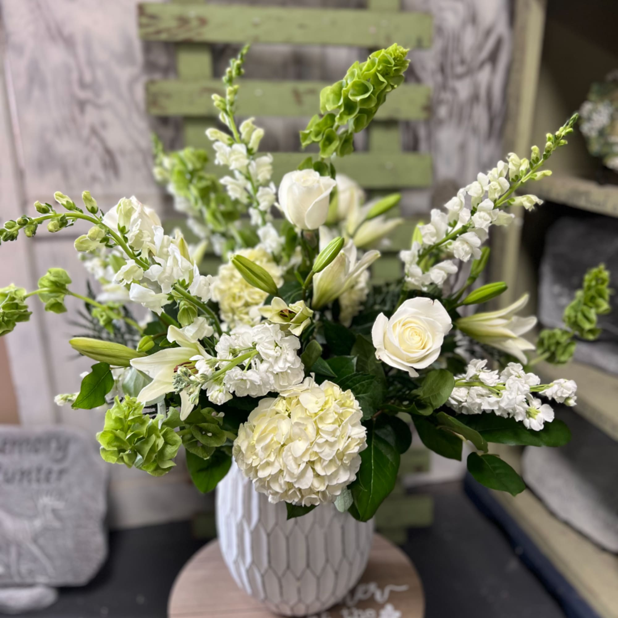 White floral arrangement in a textured vase with lilies, roses, and hydrangea