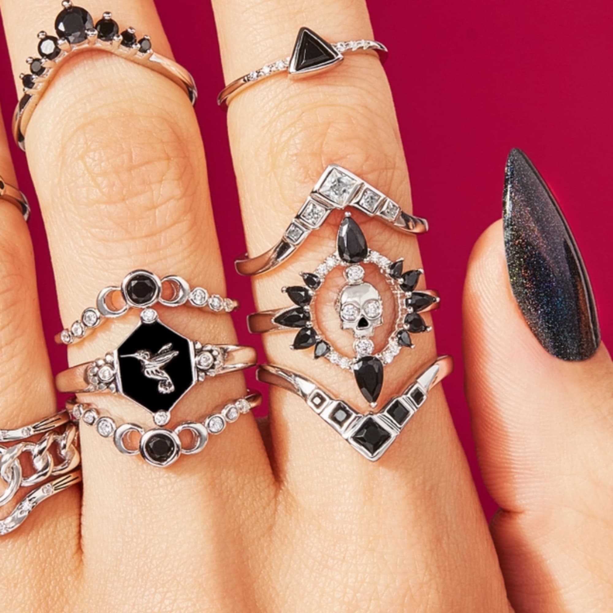 Hands wearing multiple silver rings with black stones and skull designs